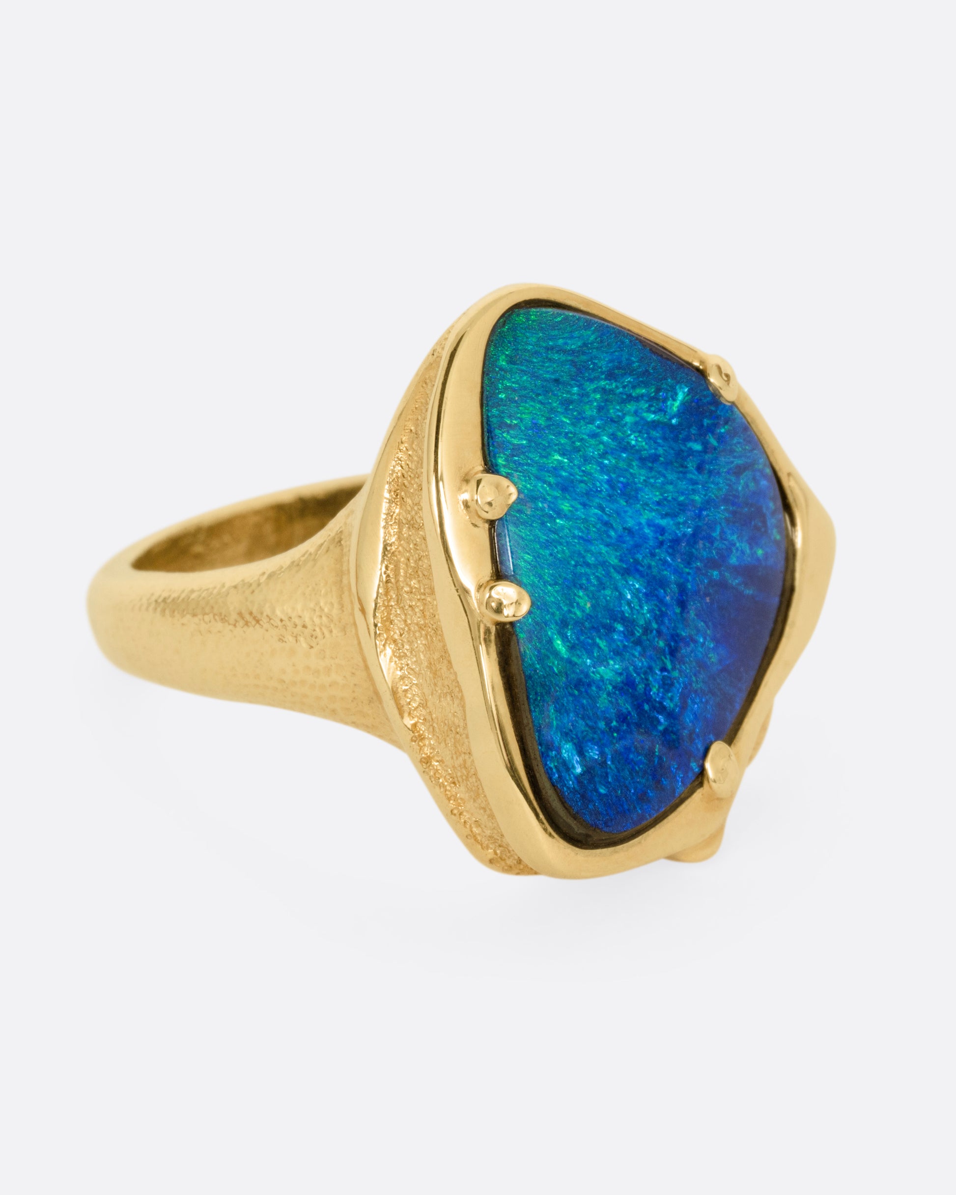 A yellow gold ring with a large boulder opal, shown from the side.