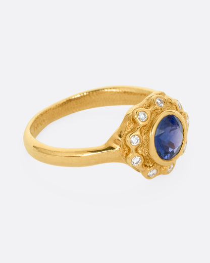 A yellow gold ring with a halo of white diamonds around a sapphire, shown from the side.