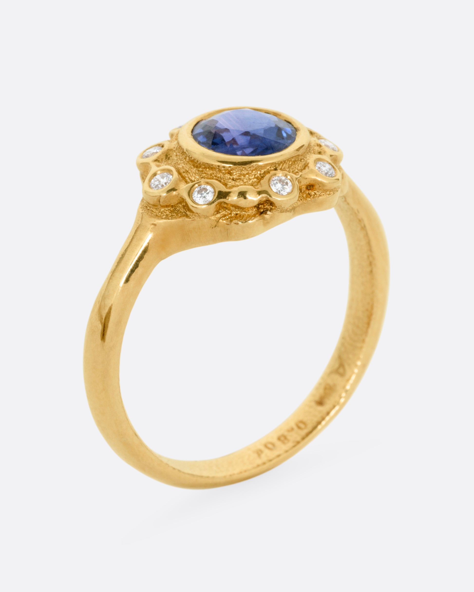 A yellow gold ring with a halo of white diamonds around a sapphire, shown from the side standing up.