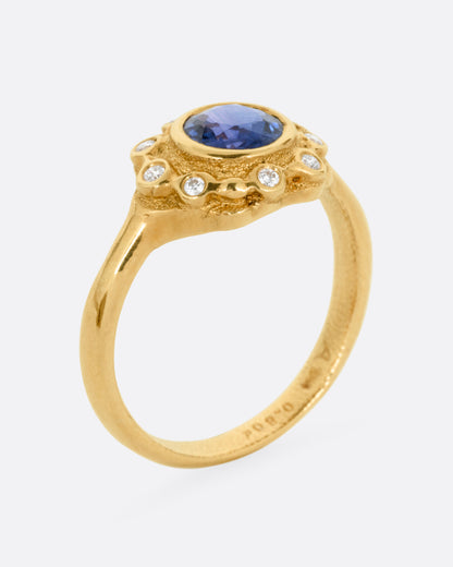 A yellow gold ring with a halo of white diamonds around a sapphire, shown from the side standing up.