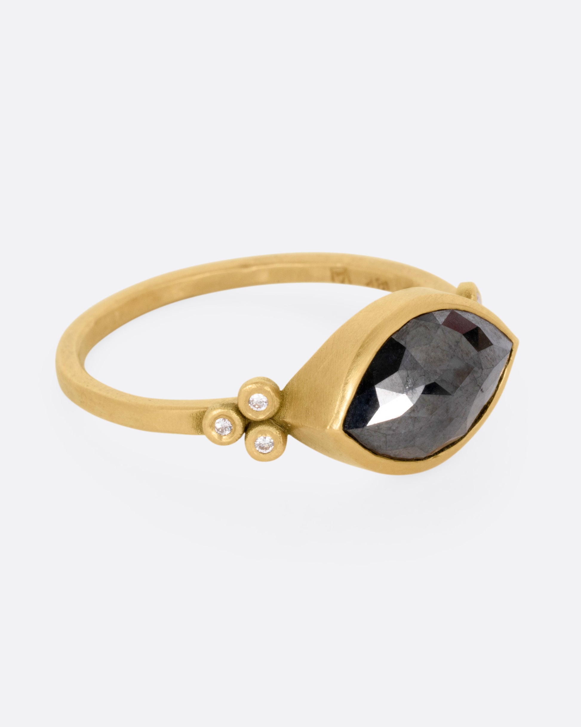 A yellow gold ring with a wide eye-shaped black marquise diamond flanked by a trio of white diamonds, shown from the side.