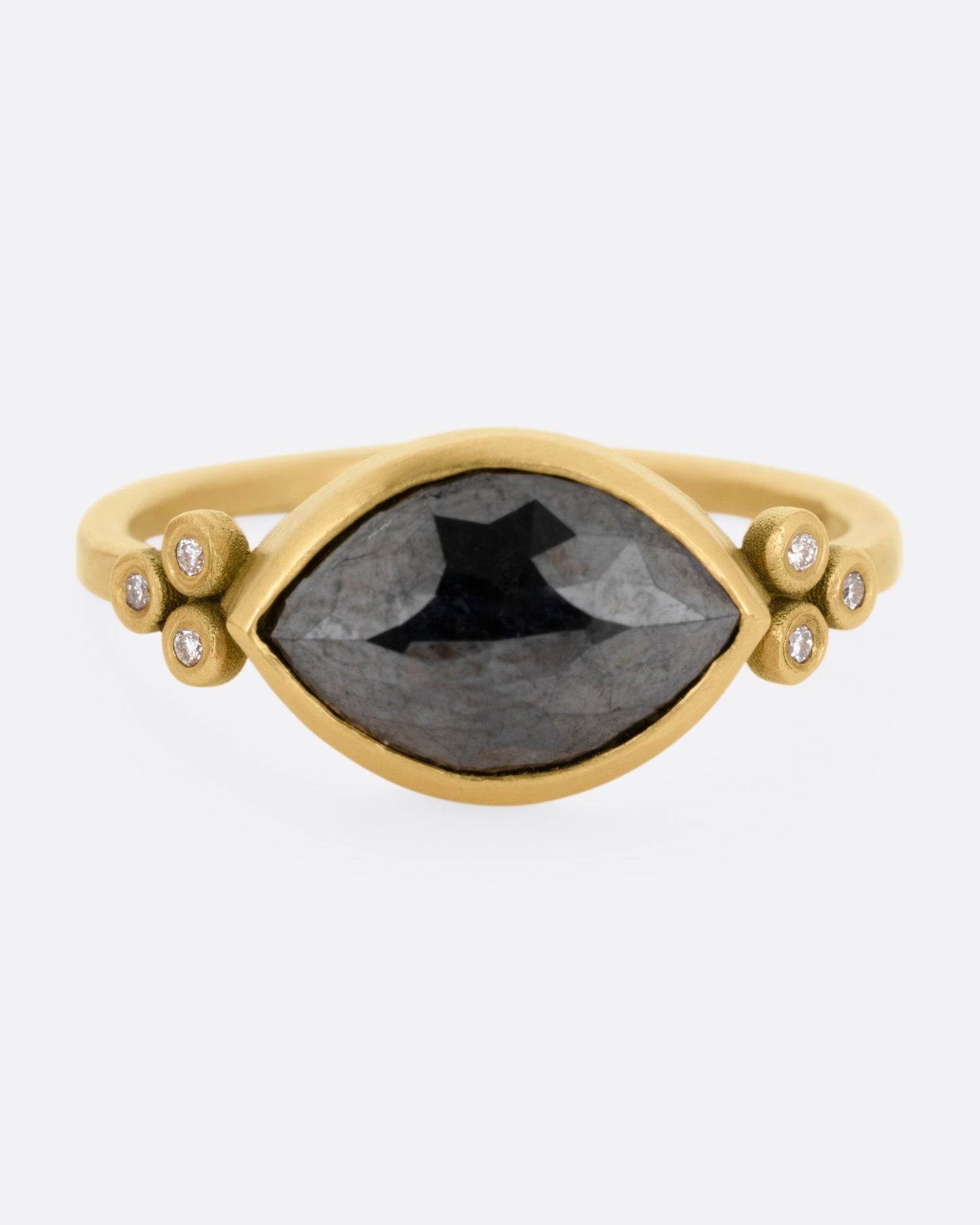 A yellow gold ring with a wide eye-shaped black marquise diamond flanked by a trio of white diamonds, shown from the front.
