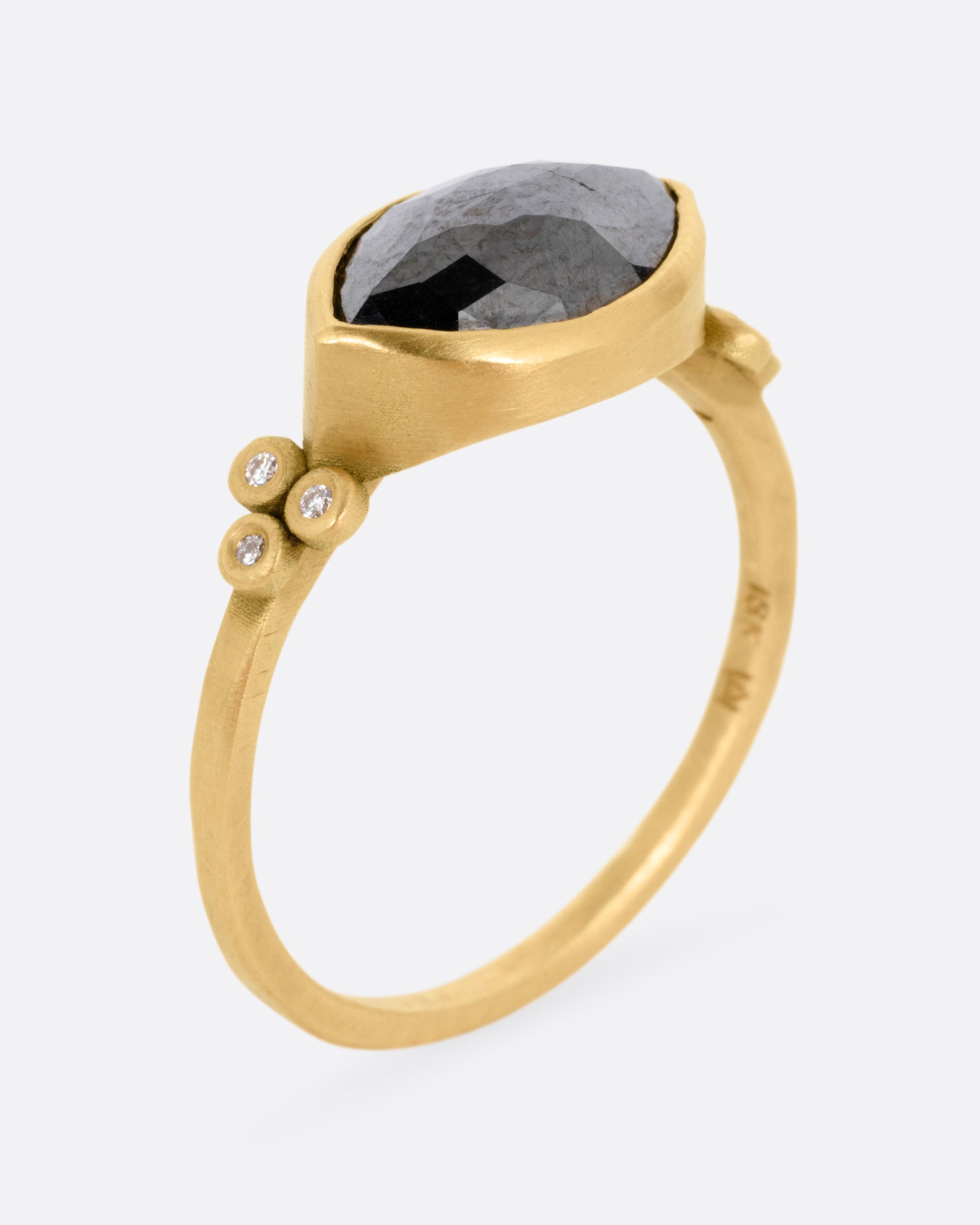 A yellow gold ring with a wide eye-shaped black marquise diamond flanked by a trio of white diamonds, shown from the side standing up.