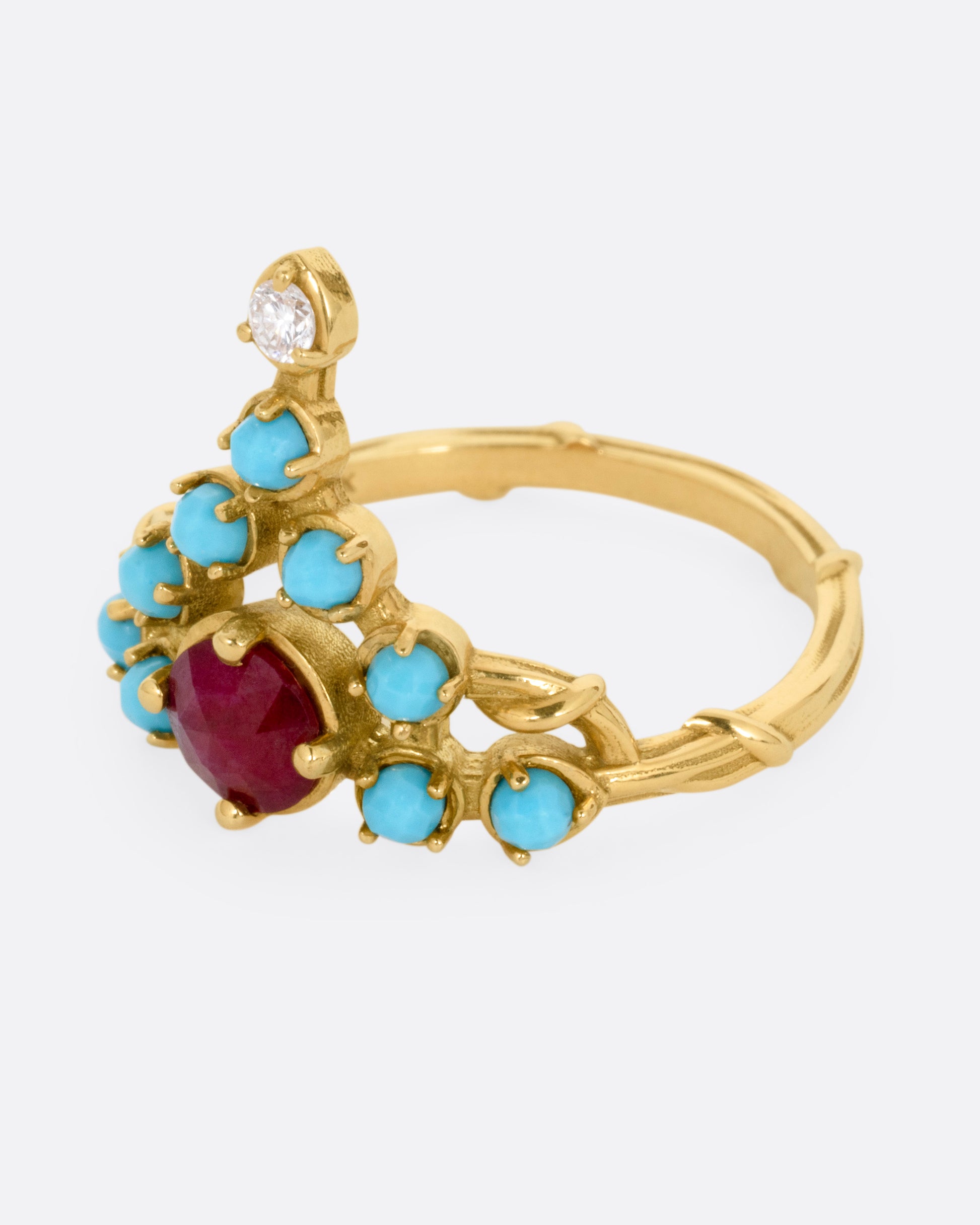 A yellow gold stacker ring with a ruby center surrounded by turquoise cabochons with a diamond tip, shown from the side.