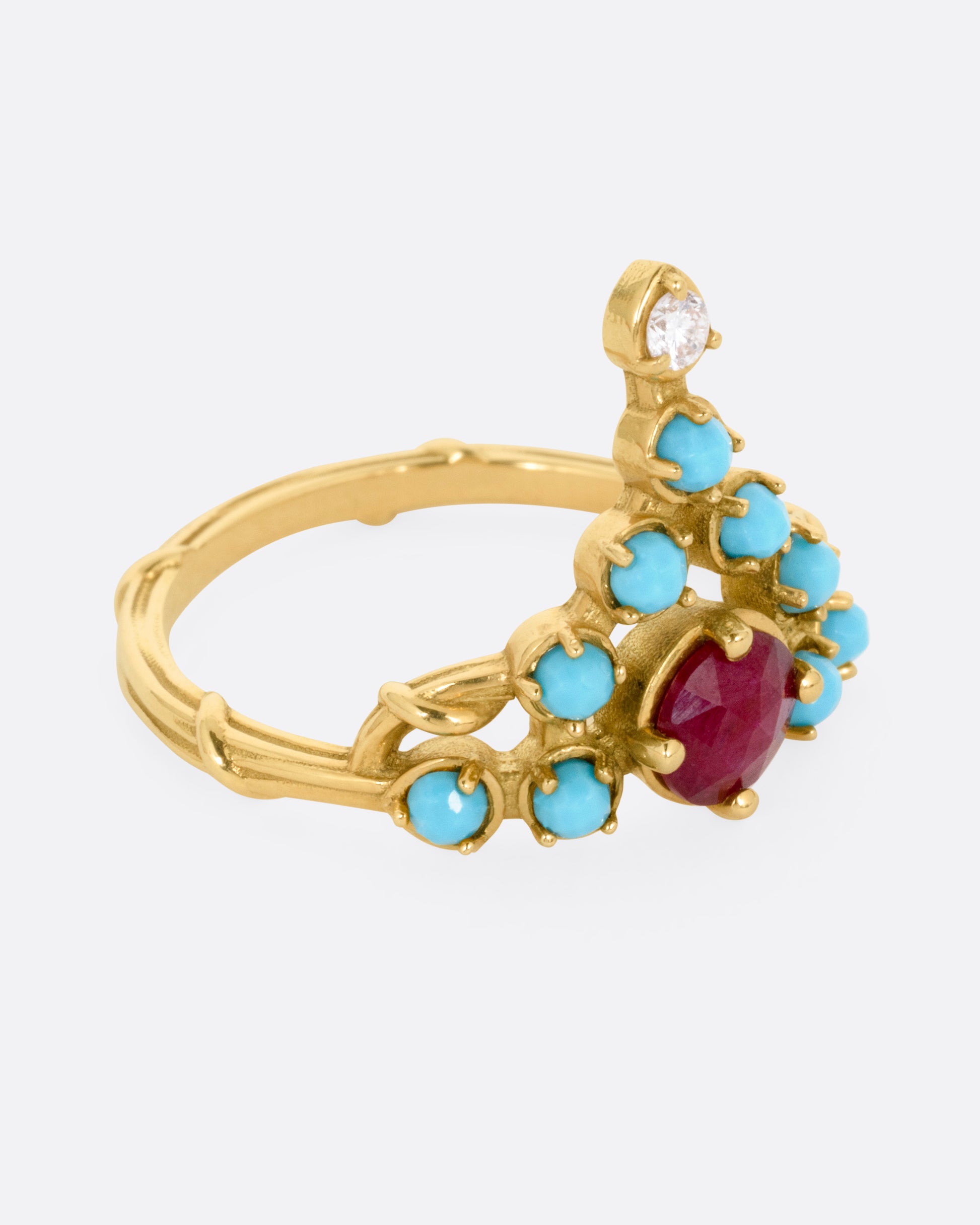 A yellow gold stacker ring with a ruby center surrounded by turquoise cabochons with a diamond tip, shown from the side.