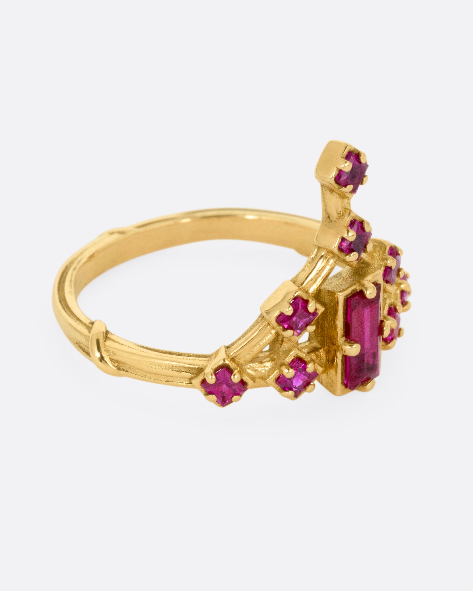 A yellow gold ring with a baguette ruby and princess cut ruby accent. Shown from the side.