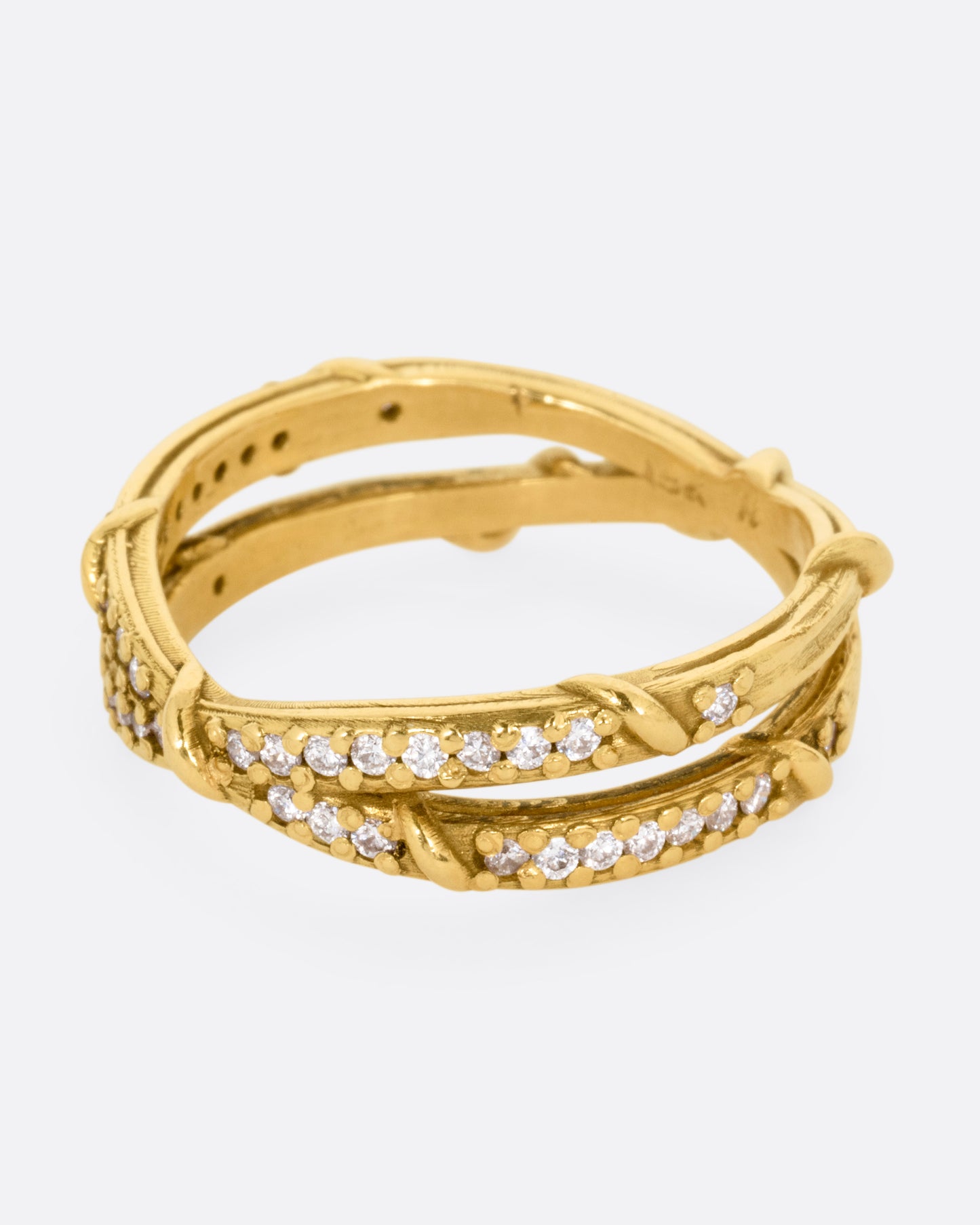 A yellow gold ring with two eternity bands intersecting at the middle and wrapped in vines and colorless diamonds. Shown from the side.