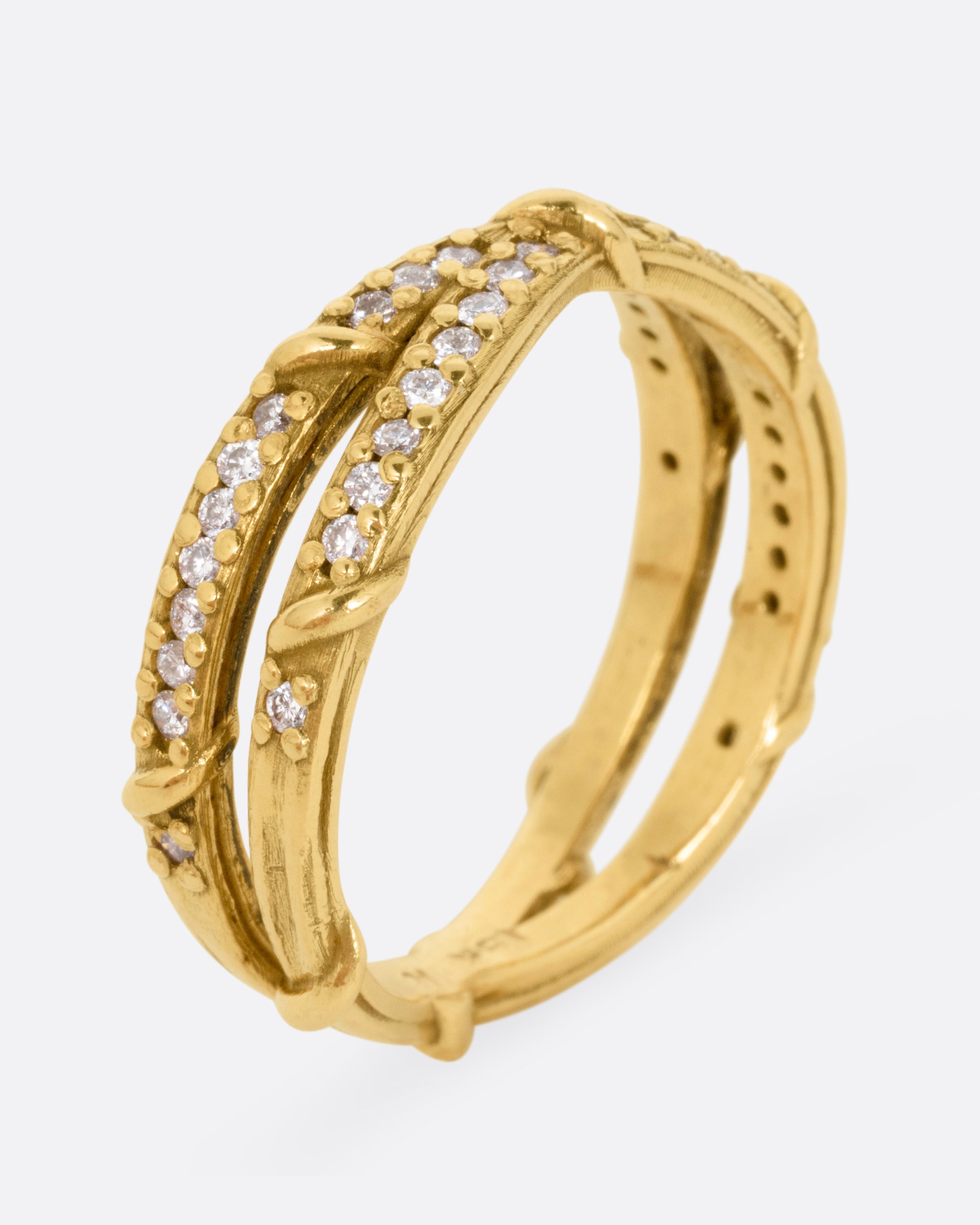 A yellow gold ring with two eternity bands intersecting at the middle and wrapped in vines and colorless diamonds. Shown standing up from the side.