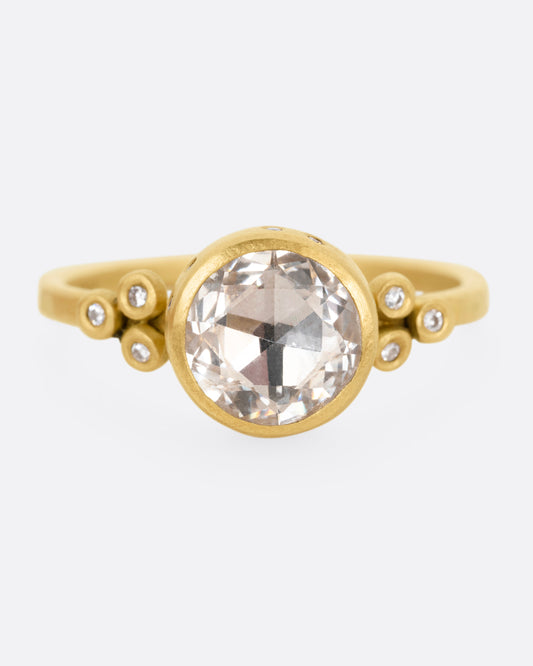 A yellow gold ring with a rose cut white sapphire bookended by diamond accents, shown from the front.
