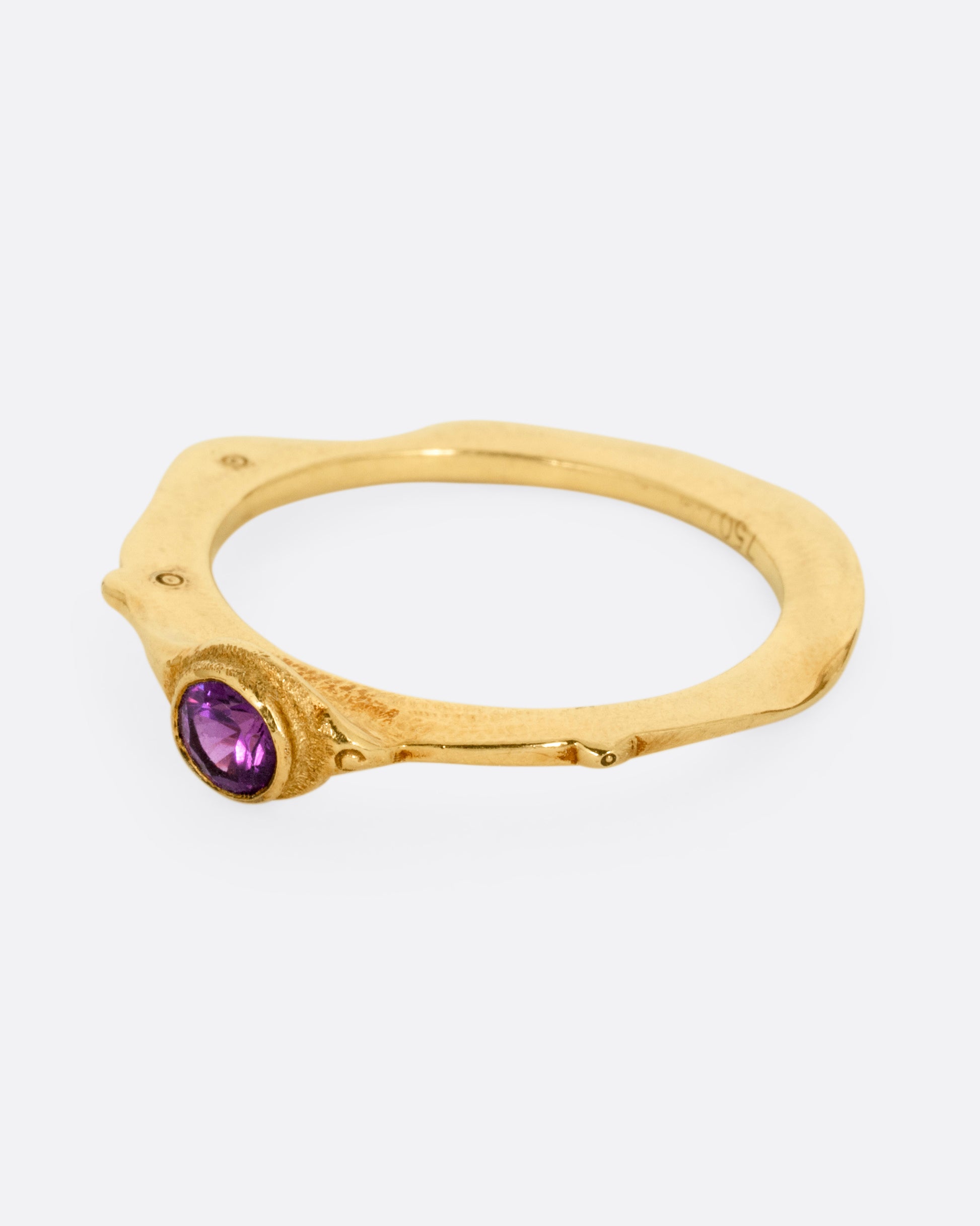 A yellow gold narrow sculptural ring with a purple sapphire, shown from the side.