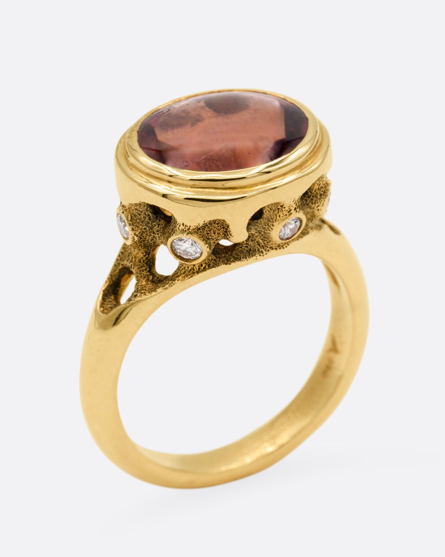 A yellow gold ring with a pink tourmaline and diamond accents. Shown from the side standing up.