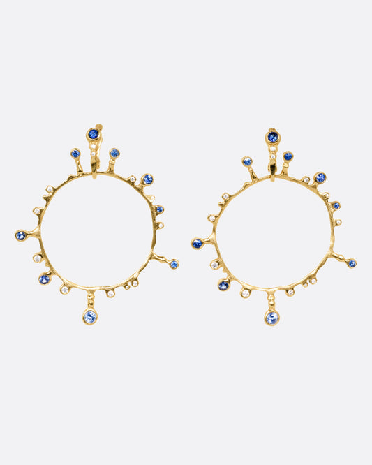 A pair of yellow gold hoop sunburst earrings with diamonds and sapphires. Shown from the front.