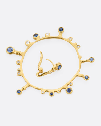A yellow gold hoop sunburst earring with diamonds and sapphires. Shown open lying on its side.