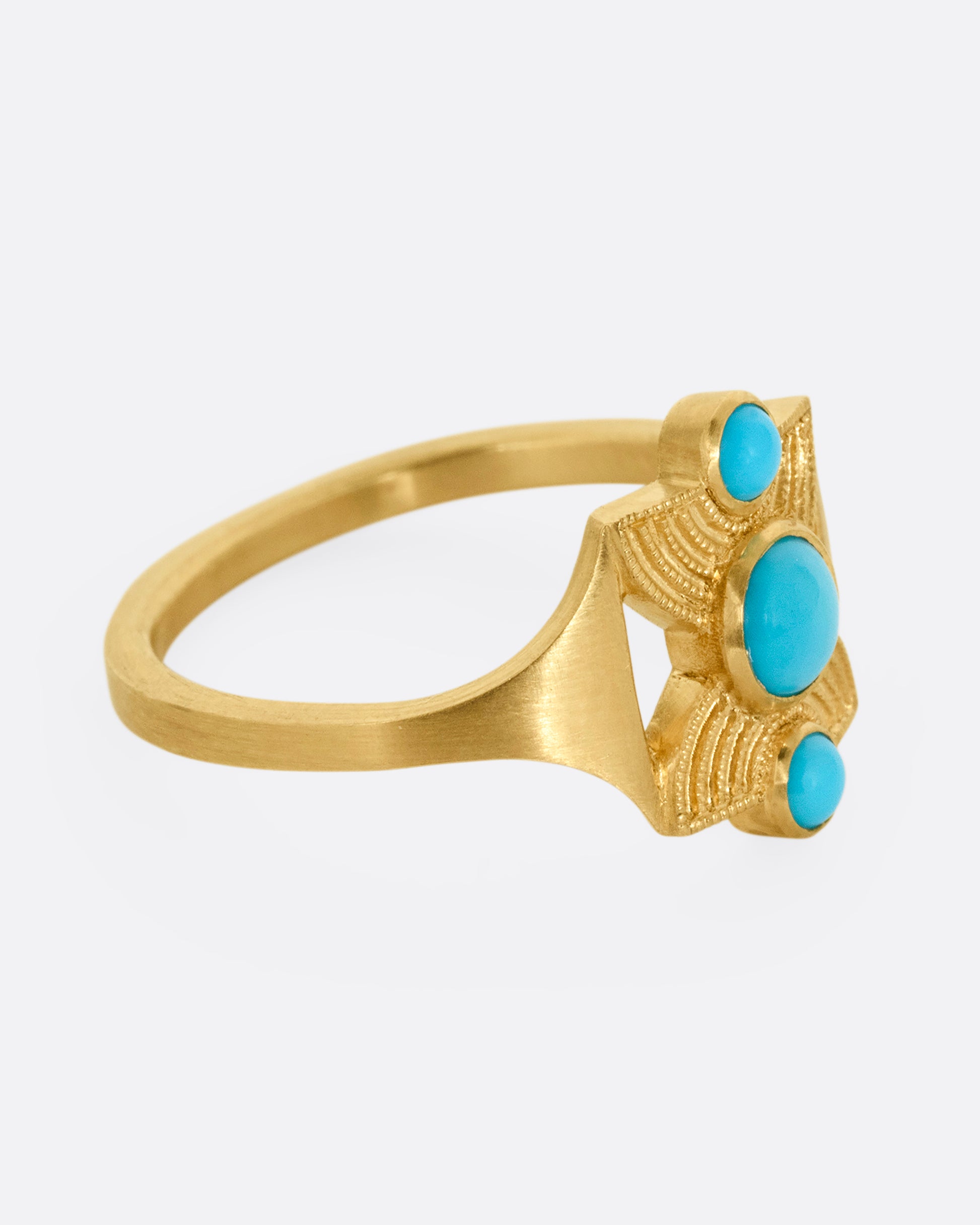 A yellow gold hourglass shaped ring with three stacked bezel set turquoises. Shown from the side.