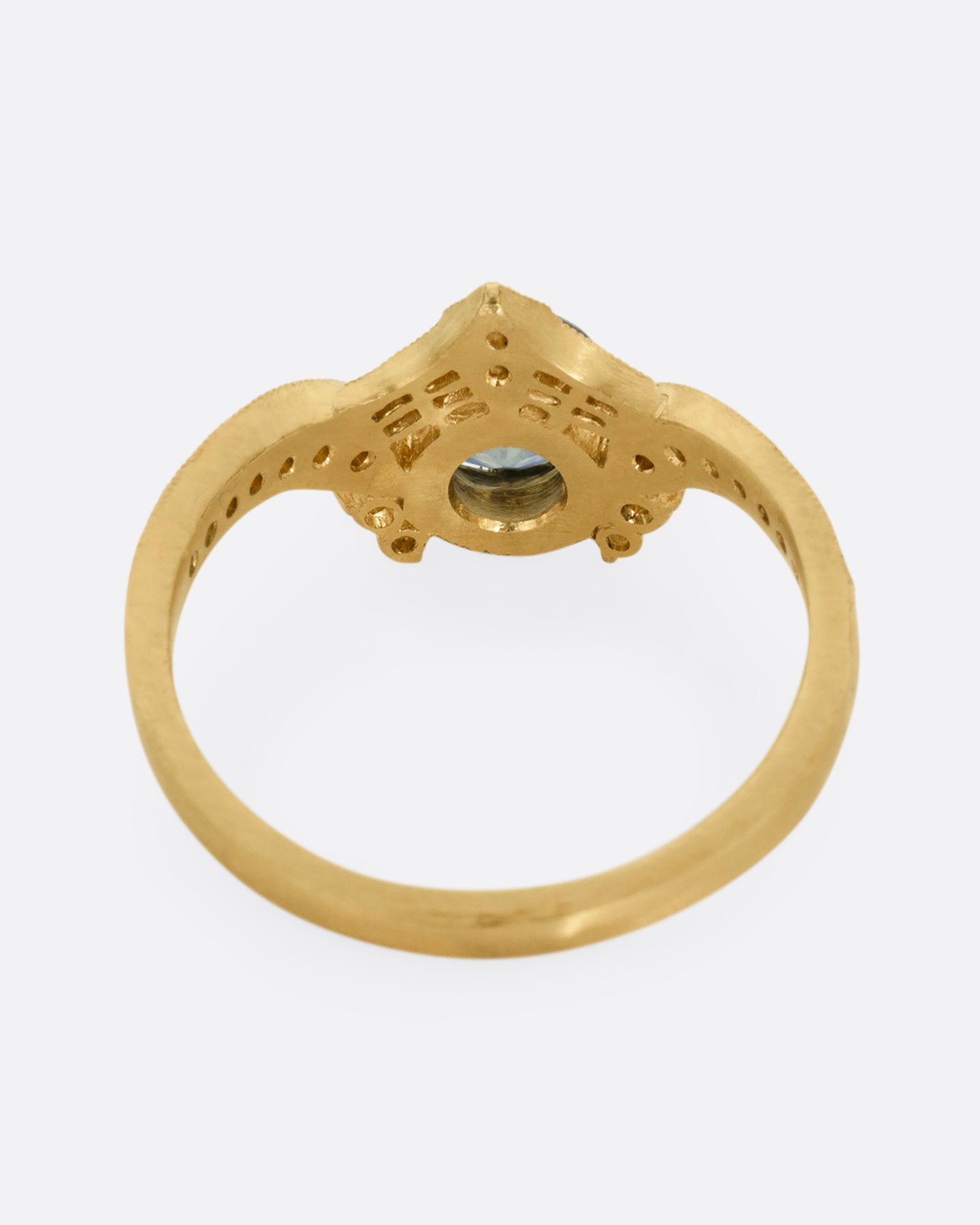 A yellow gold ring with a prong set teal sapphire, delicate cutouts, and white diamond accents. Shown from the back.