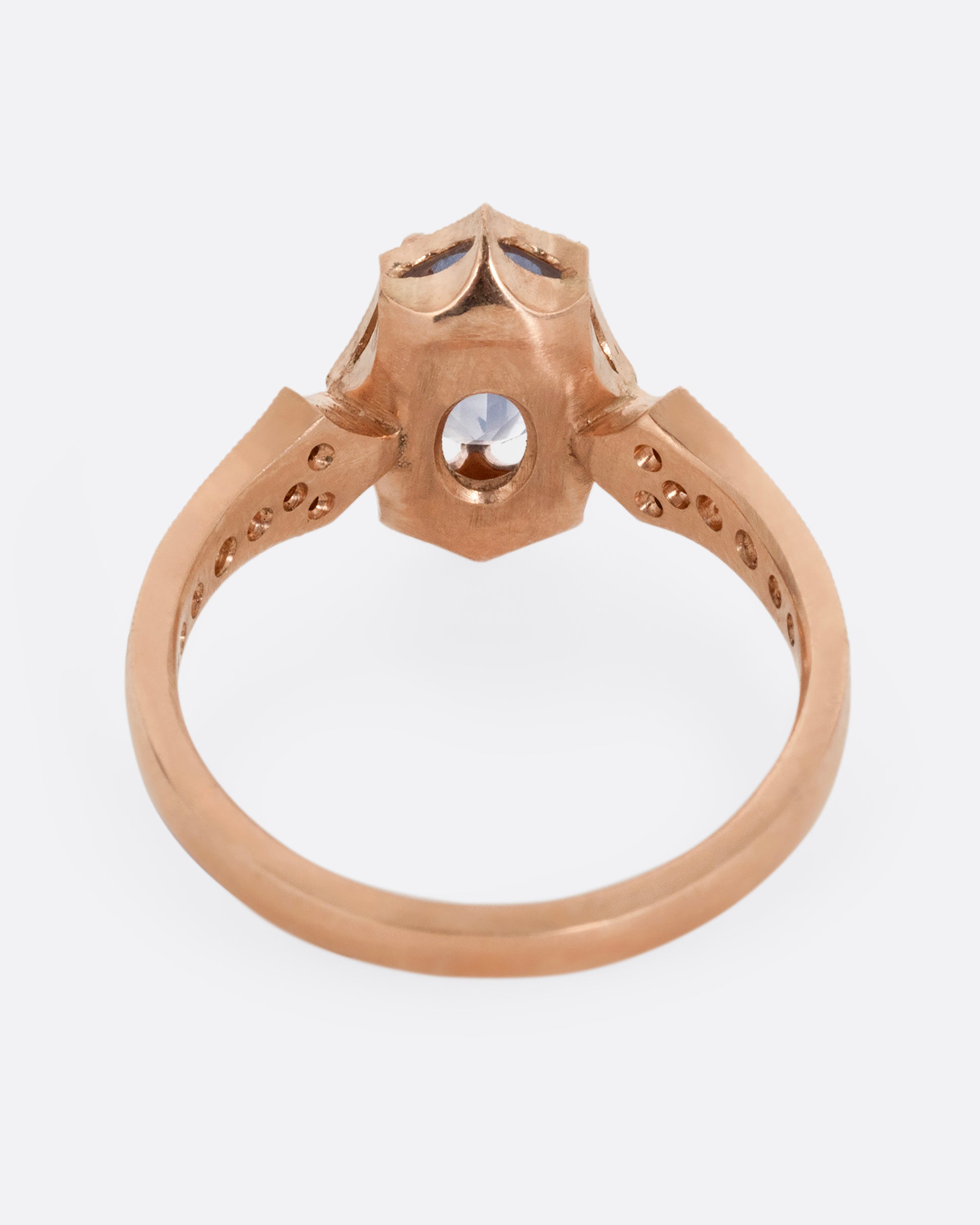 A rose gold ring with a prong set lavender sapphire at the center and diamond lined shoulders. Shown from the back.
