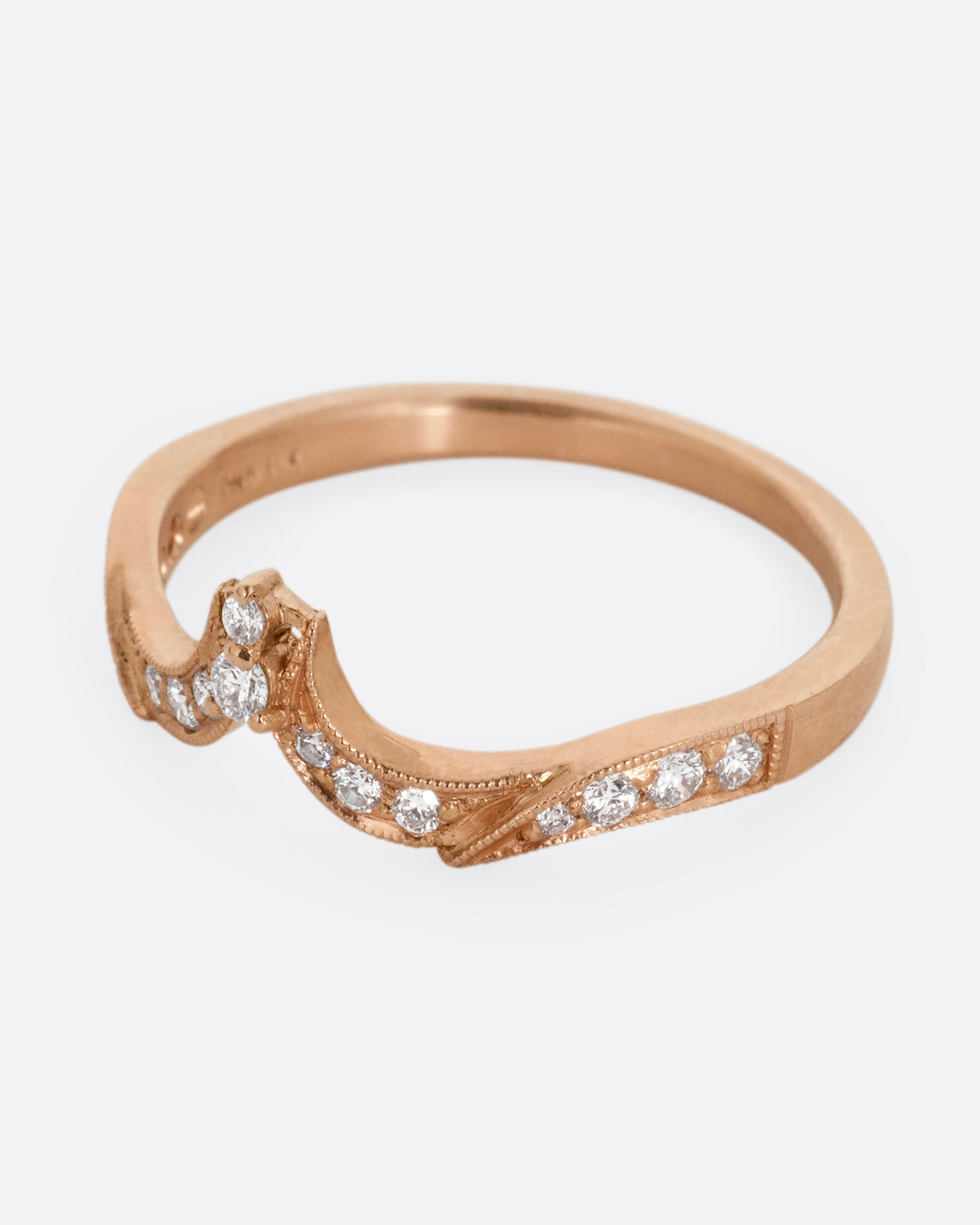 A rose gold ring with tapering curves of pavé diamonds that come to a point at the center. Shown from the side.