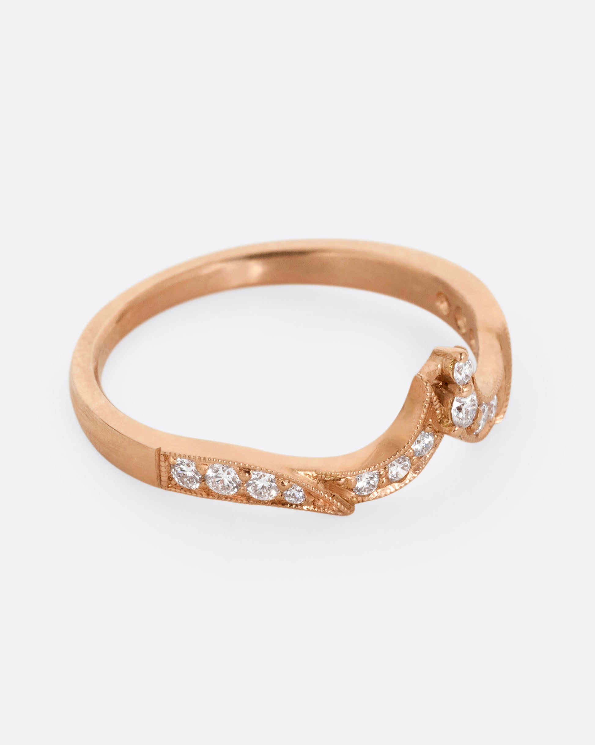 A rose gold ring with tapering curves of pavé diamonds that come to a point at the center. Shown from the side.