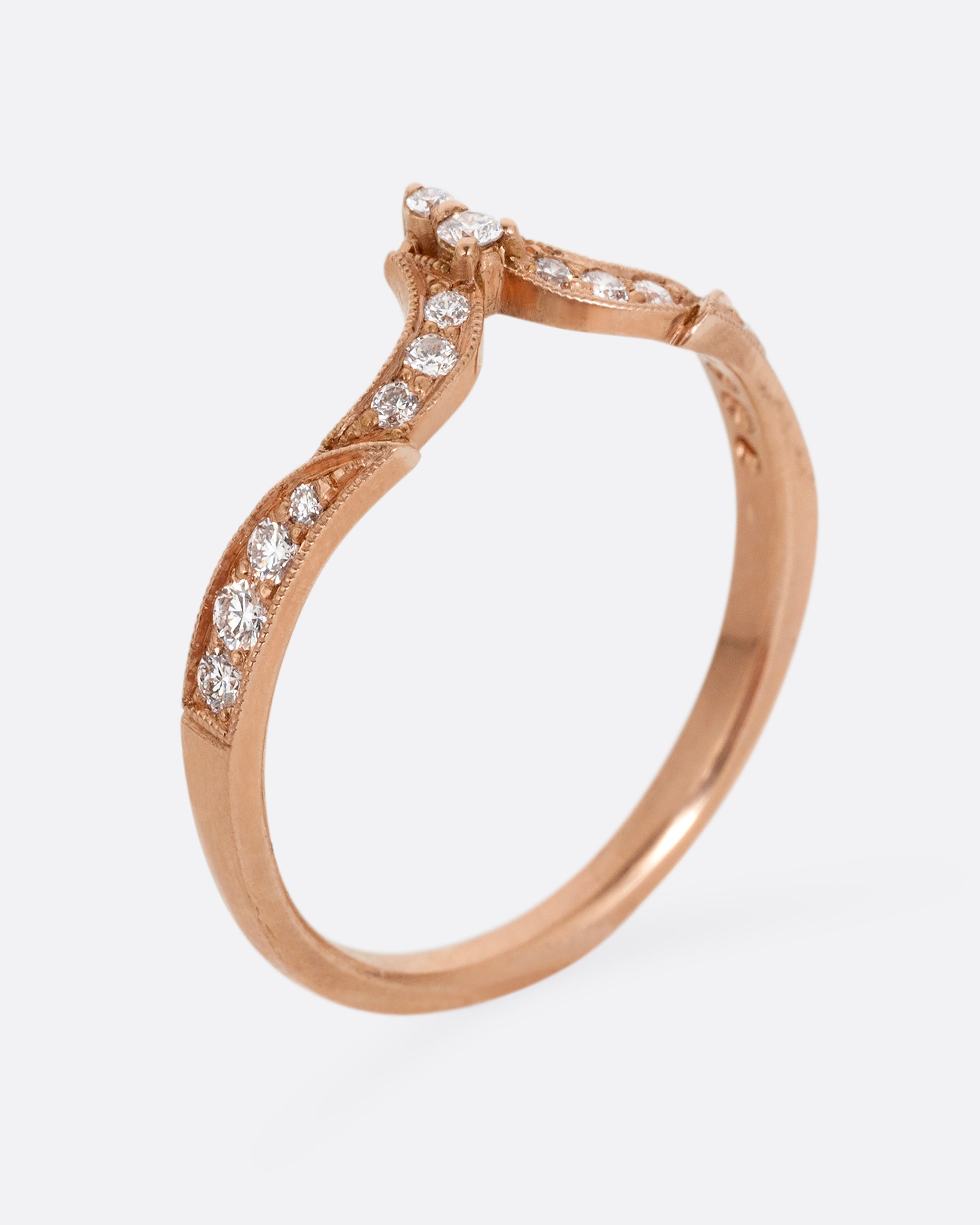 A rose gold ring with tapering curves of pavé diamonds that come to a point at the center. Shown standing up from the side.