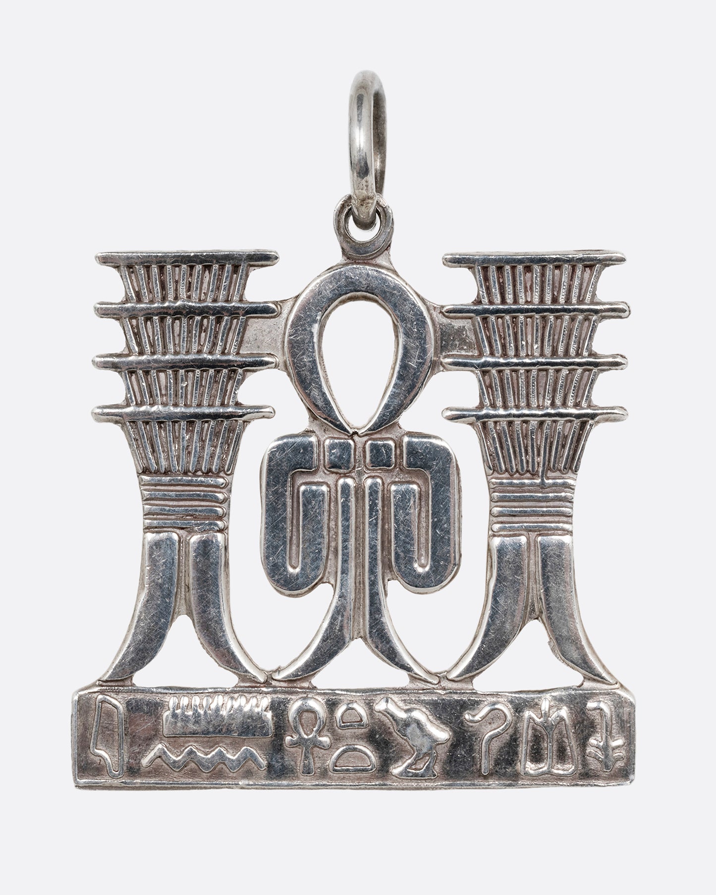 A silver pendant with Egyptian symbols of Sa and Djed with hieroglyphs along the bottom. Shown from the front.