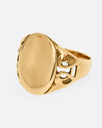 A yellow gold ring with an oval face and an ornate band, shown from the side.