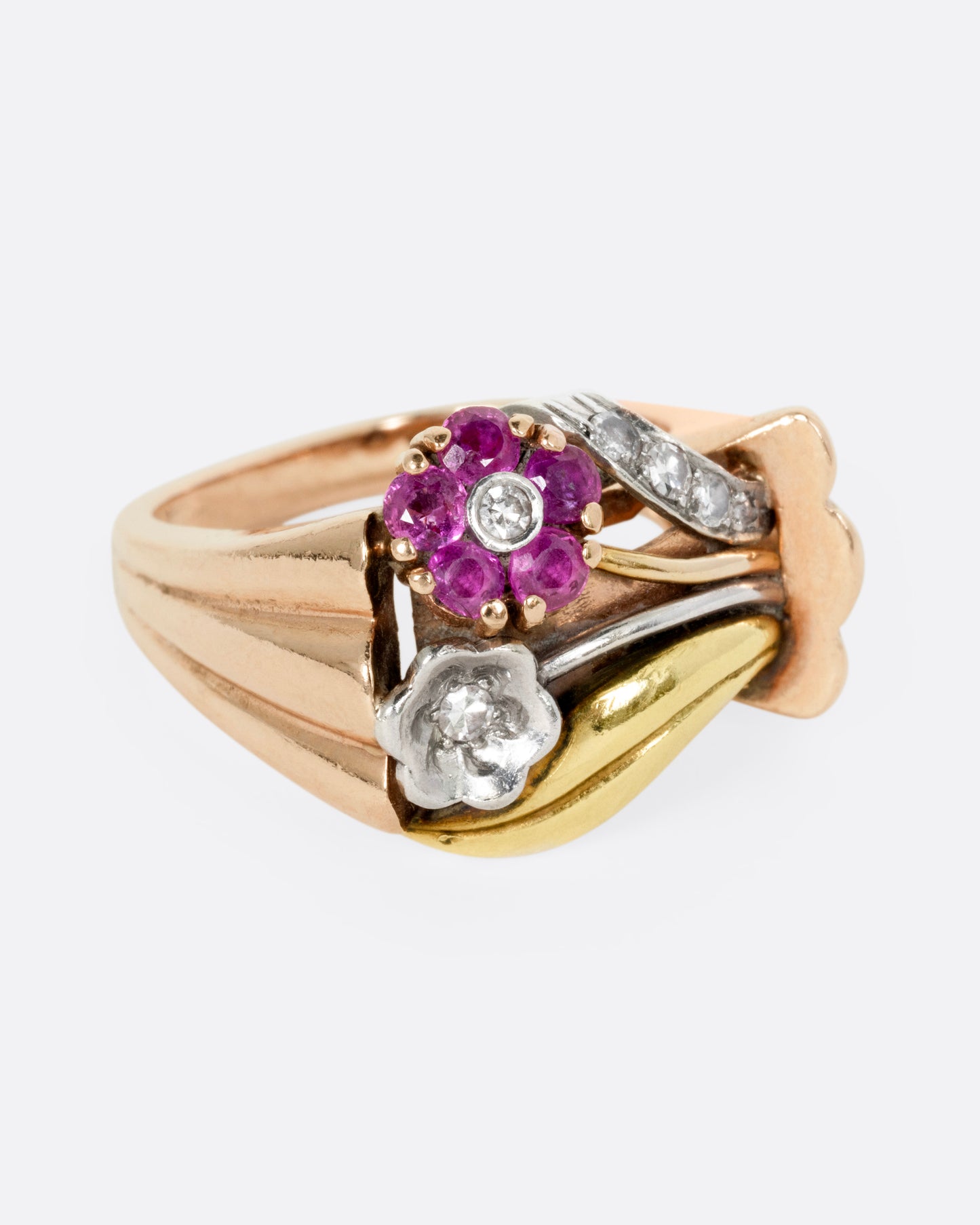 A yellow, white, and rose gold ring with ruby and diamond flowers and diamond details, shown from the front.