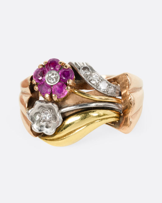 A yellow, white, and rose gold ring with ruby and diamond flowers and diamond details, shown from the front.
