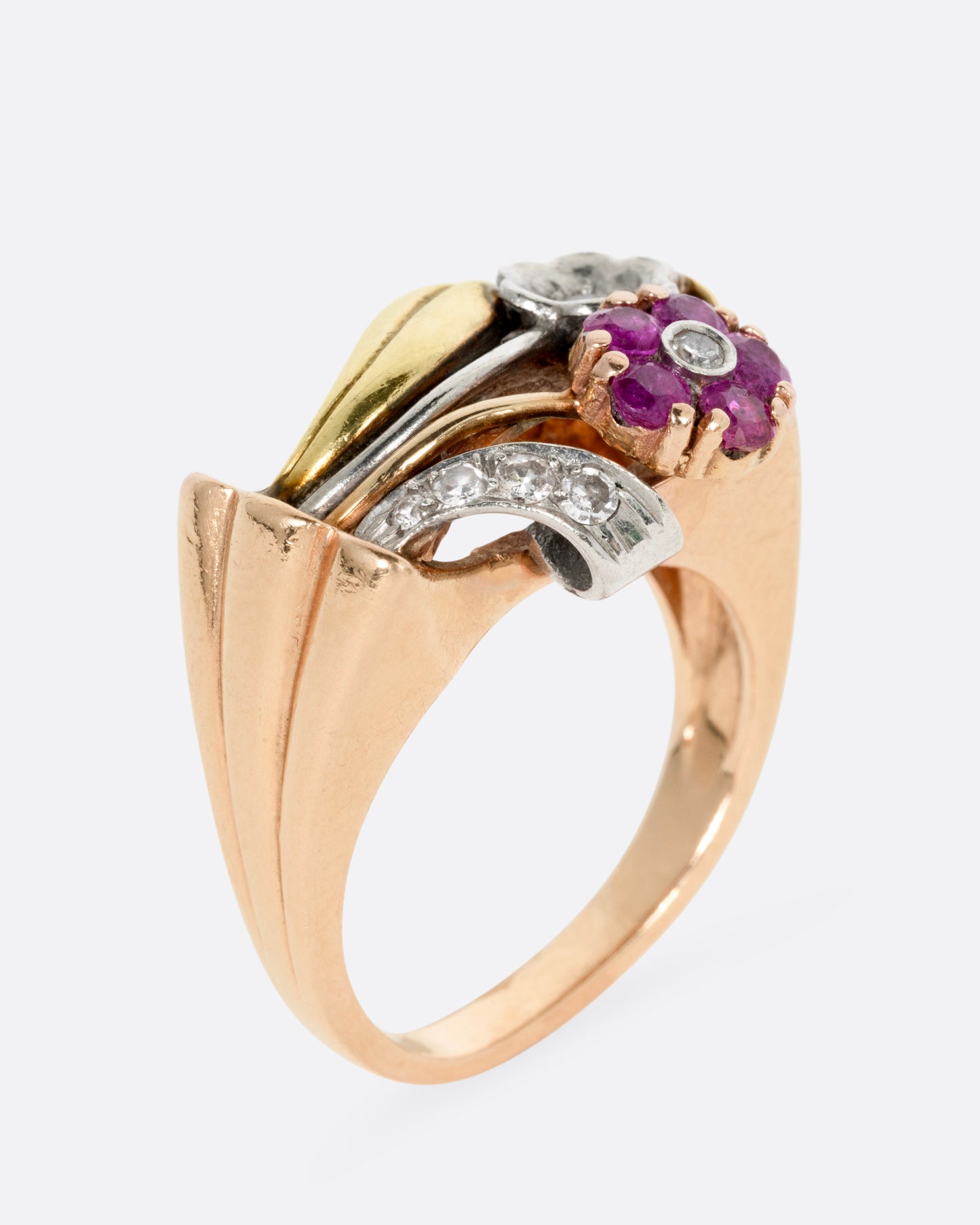 A yellow, white, and rose gold ring with ruby and diamond flowers and diamond details, shown standing up from the side.
