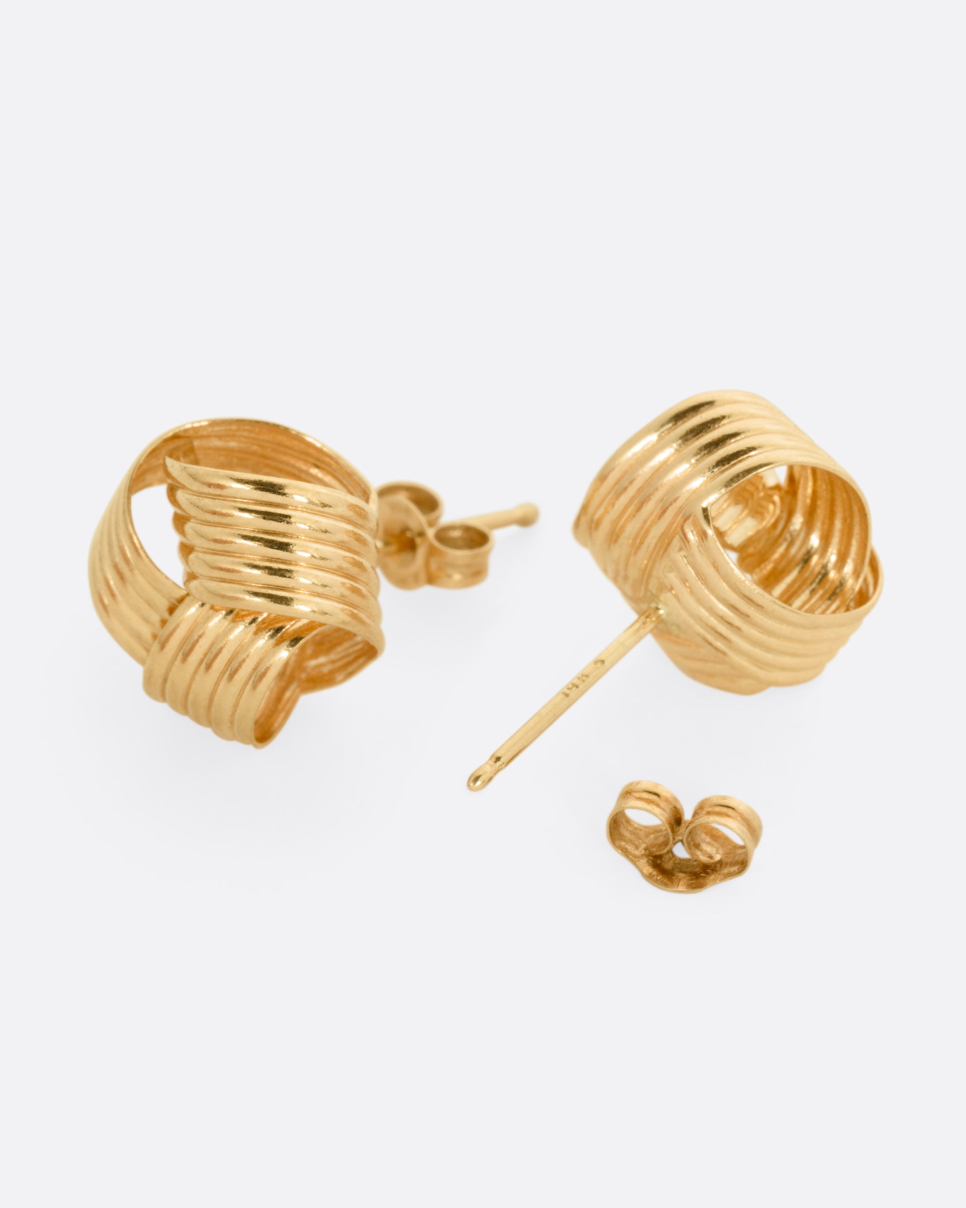 A pair of knot shaped yellow gold stud earrings. One earring is shown from the front, the other is open from the back.
