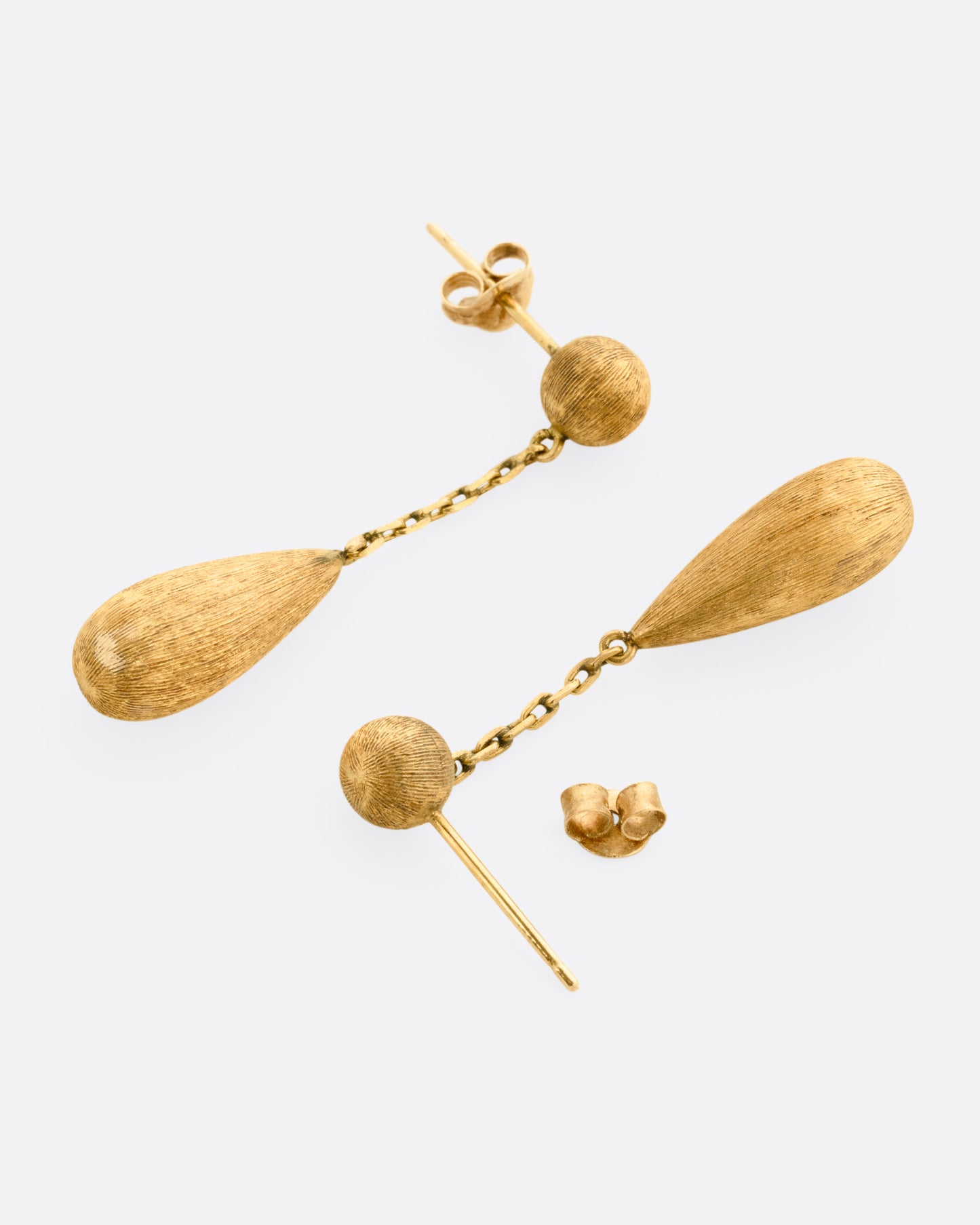 A pair of yellow gold teardrop shaped earrings, shown lying on their sides with one earring open.