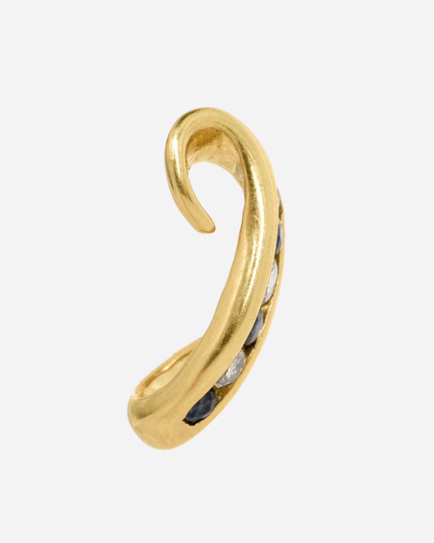 A yellow gold scroll shaped earring with a queue of channel set diamonds and sapphires, shown from the side.