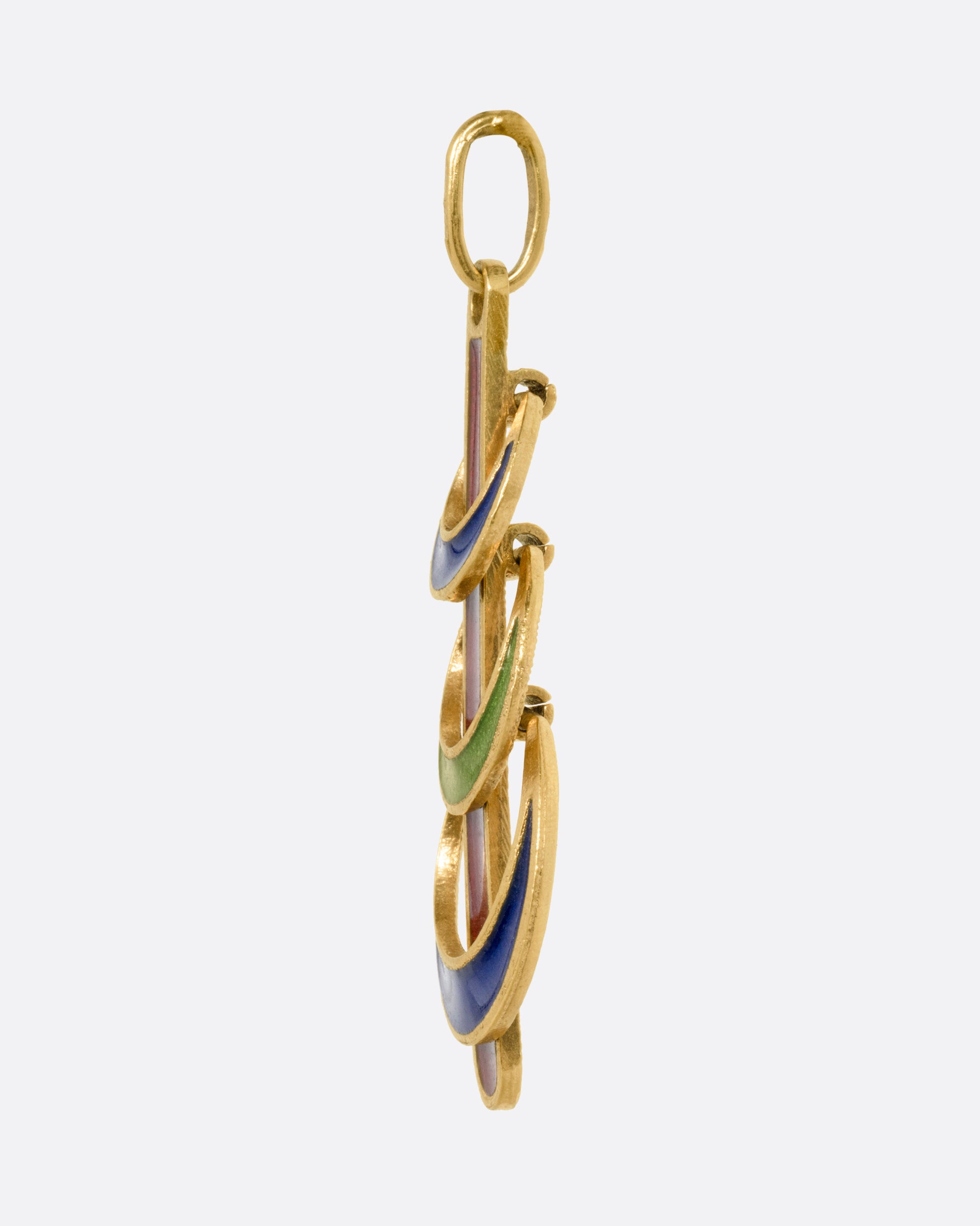 A yellow gold pendant with  three enamel crescents in blue and green on a red enamel bar. Shown from the side.