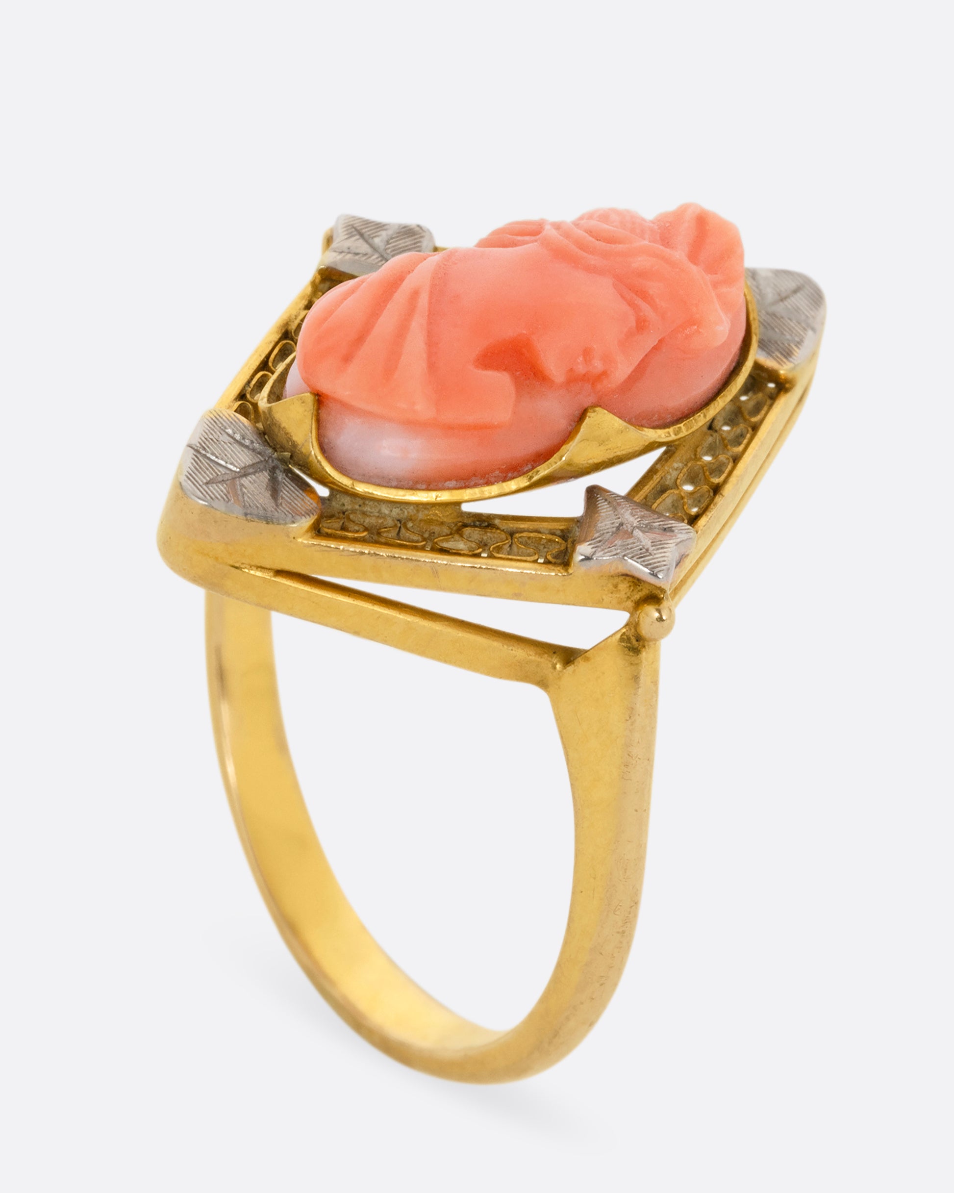 A yellow gold cameo ring with a coral carved portrait. Shown standing up from the side.