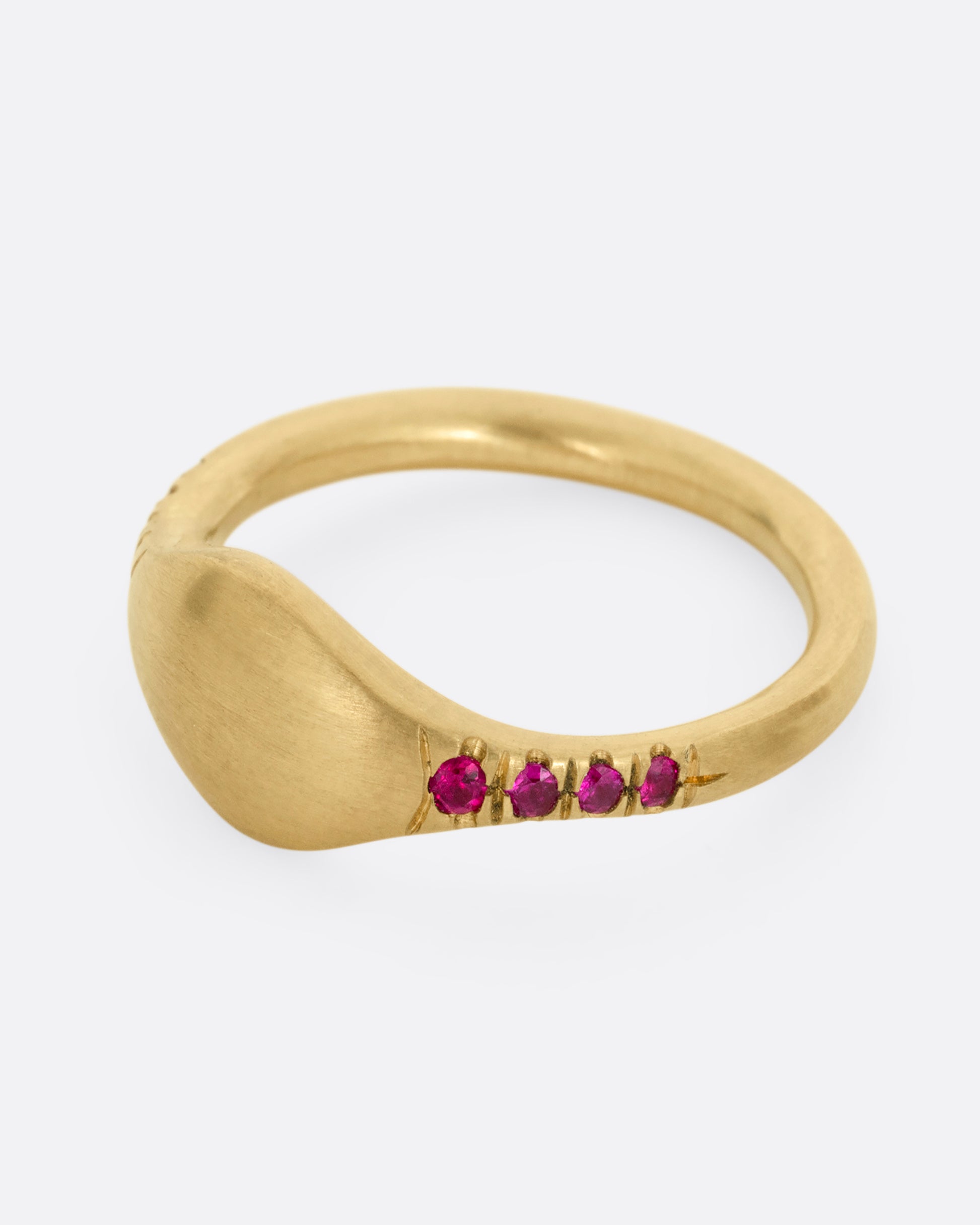 A yellow gold signet ring with rubies on the shoulders. Shown from the side.
