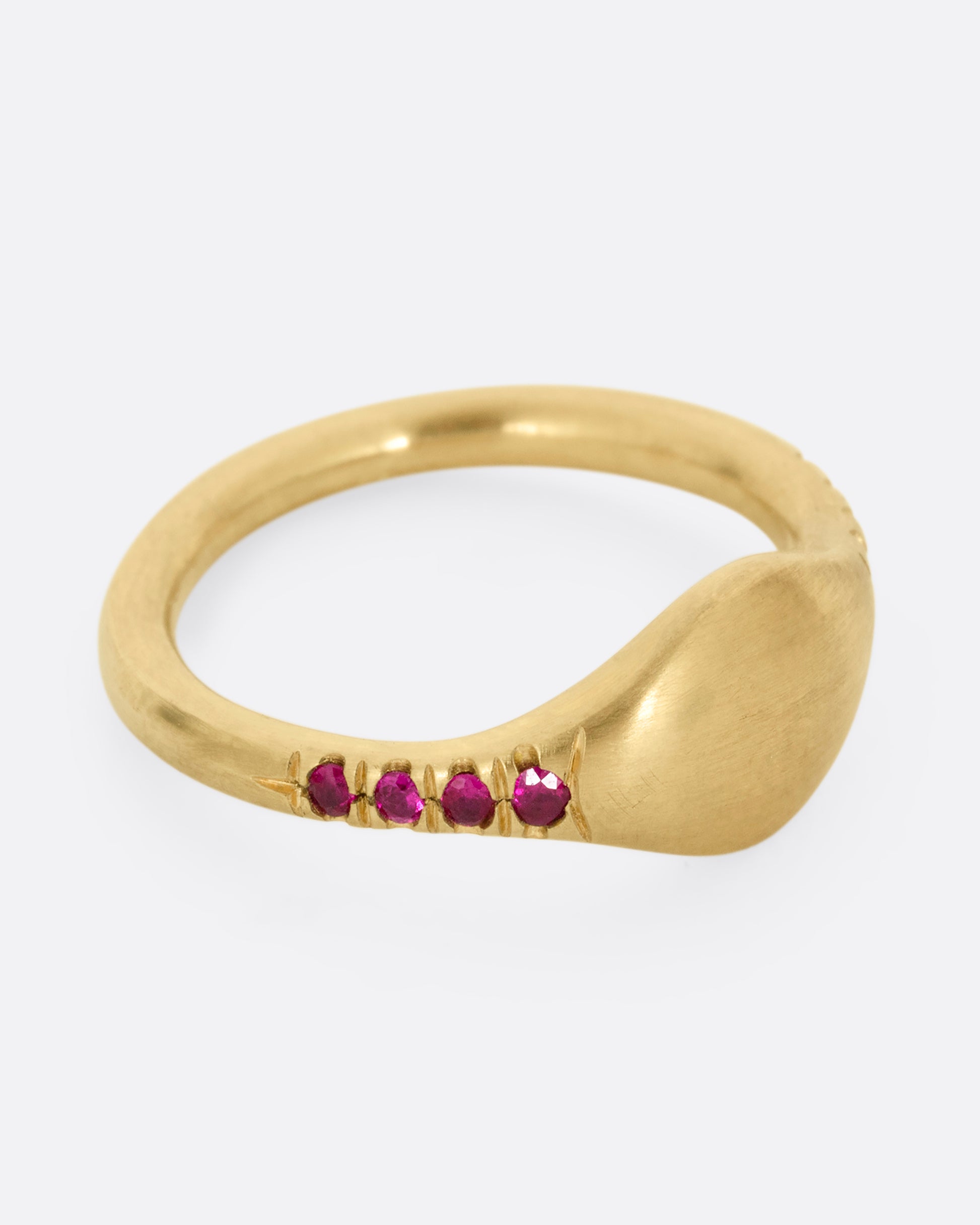 A yellow gold signet ring with rubies on the shoulders. Shown from the side.