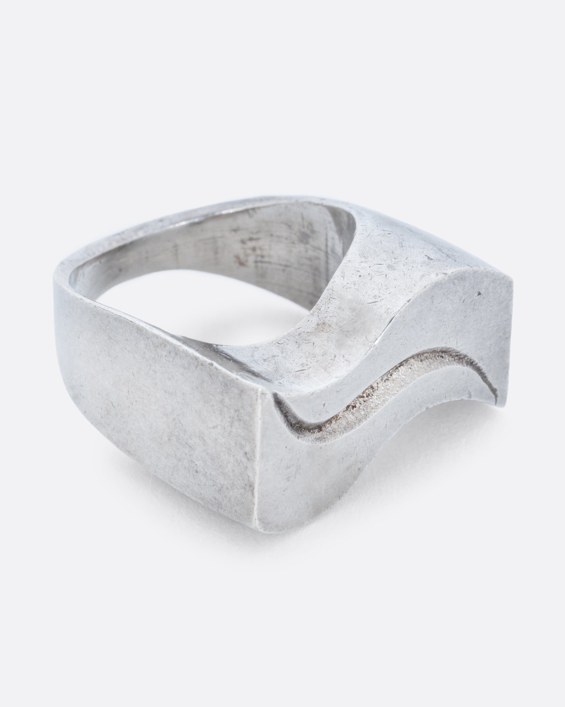 A silver ring with two waves on its face. Shown from the side.