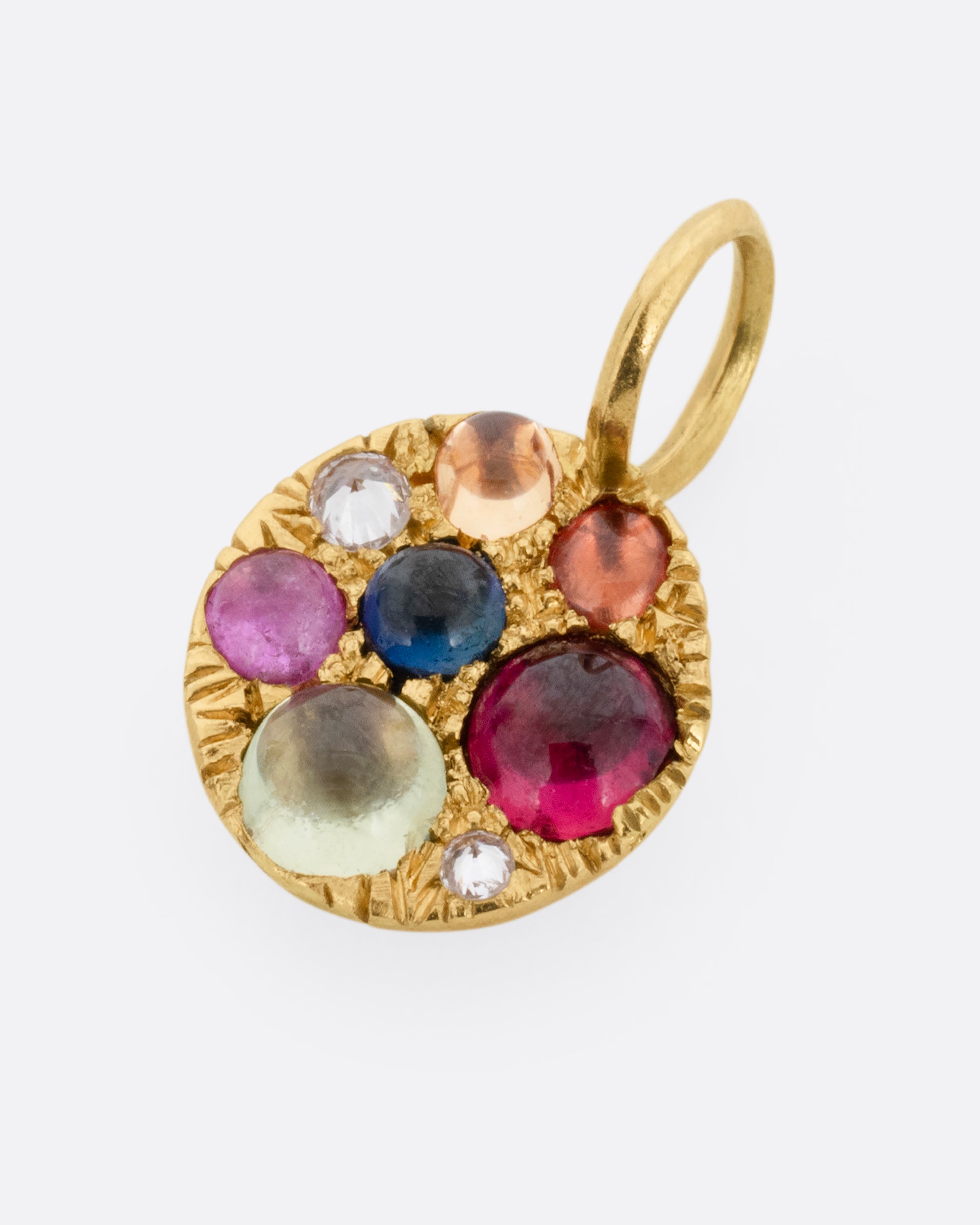 A yellow gold medallion pendant with multicolored sapphire cabochons and reverse set diamonds. Shown lying flat from the front.