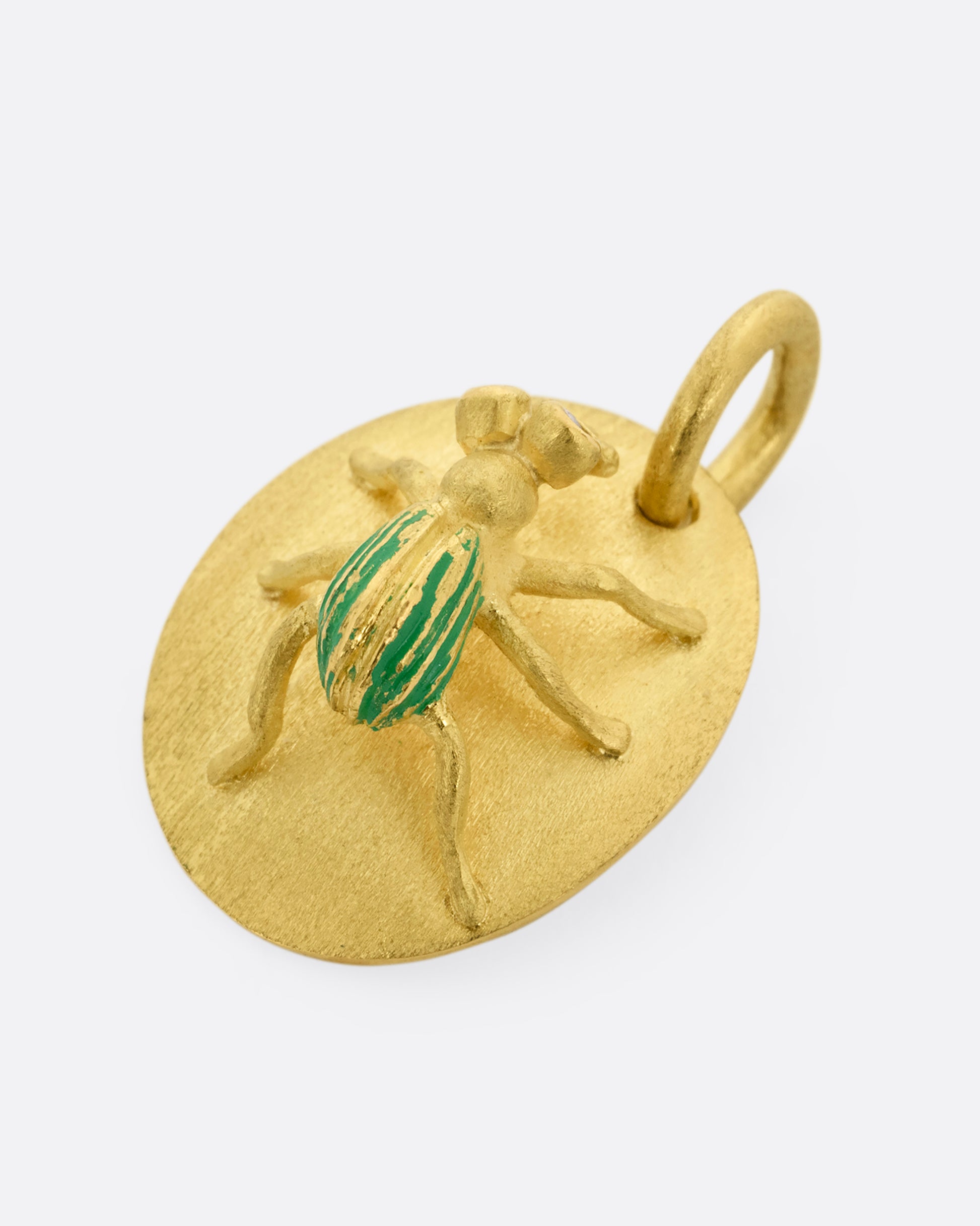 A yellow gold medallion with a diamond eyed bug with green enamel striped wings. Shown lying flat.