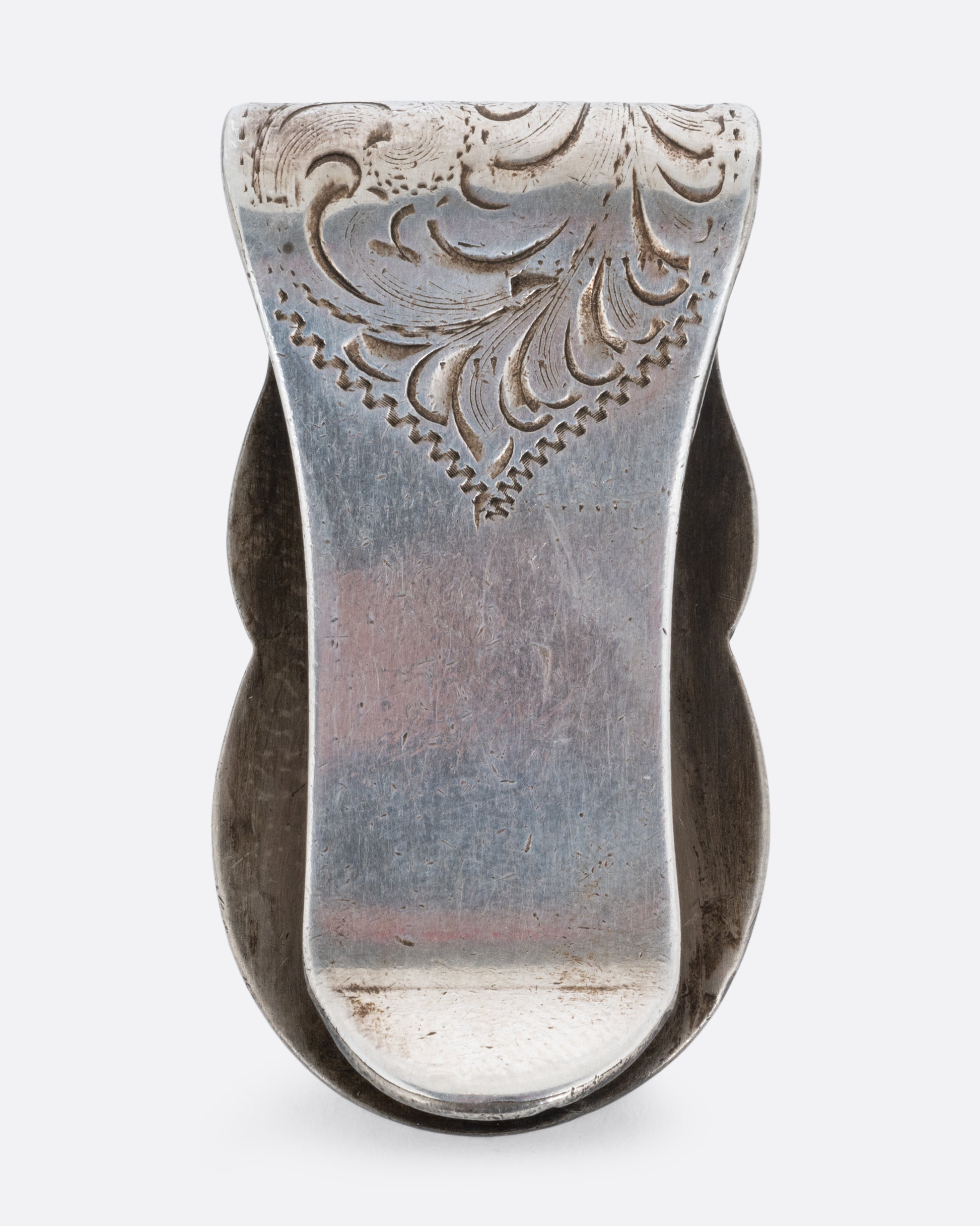 A silver money clip with a swirling engraved pattern shown from the back.