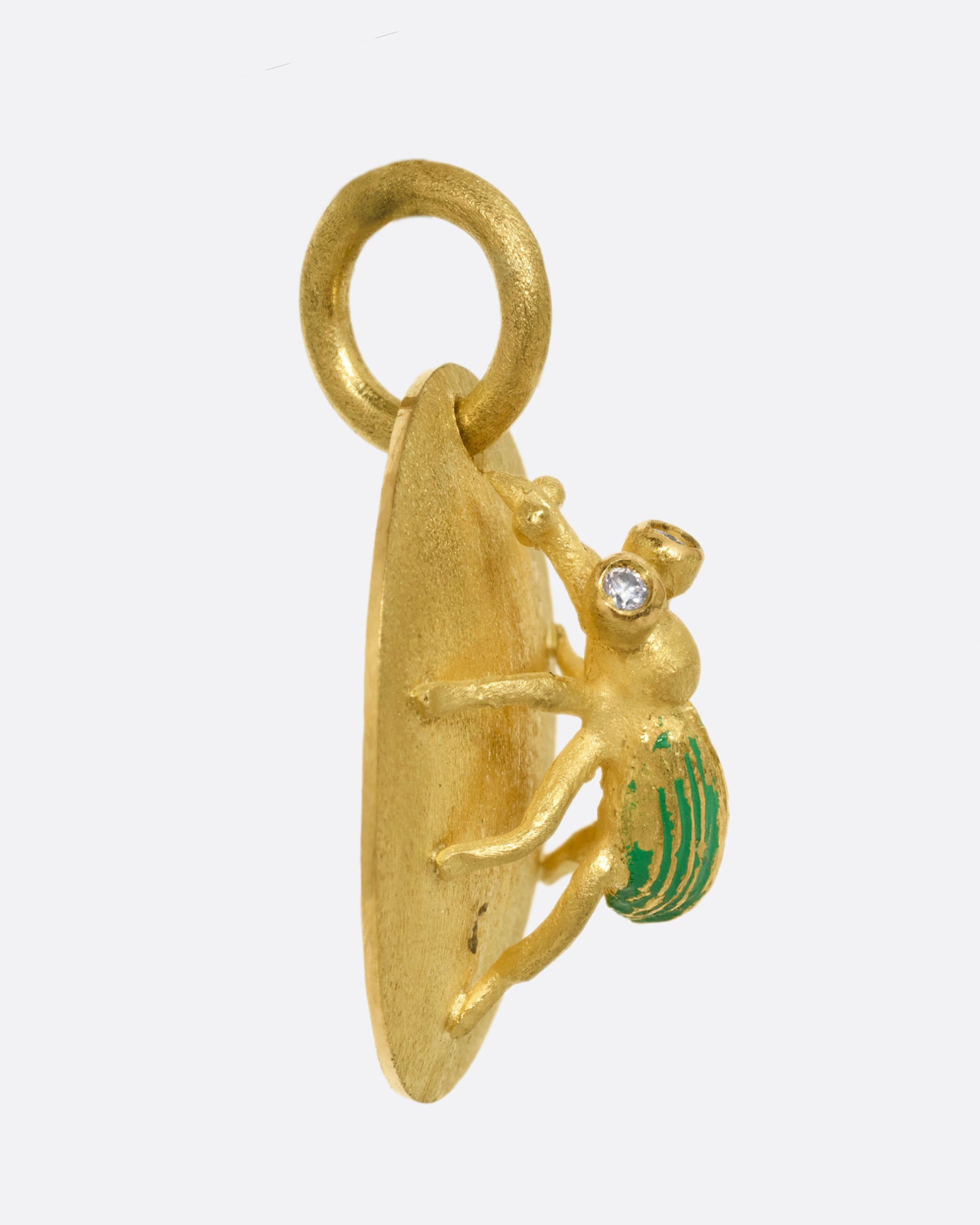 A yellow gold medallion with a diamond eyed bug with green enamel striped wings. Shown from the side.