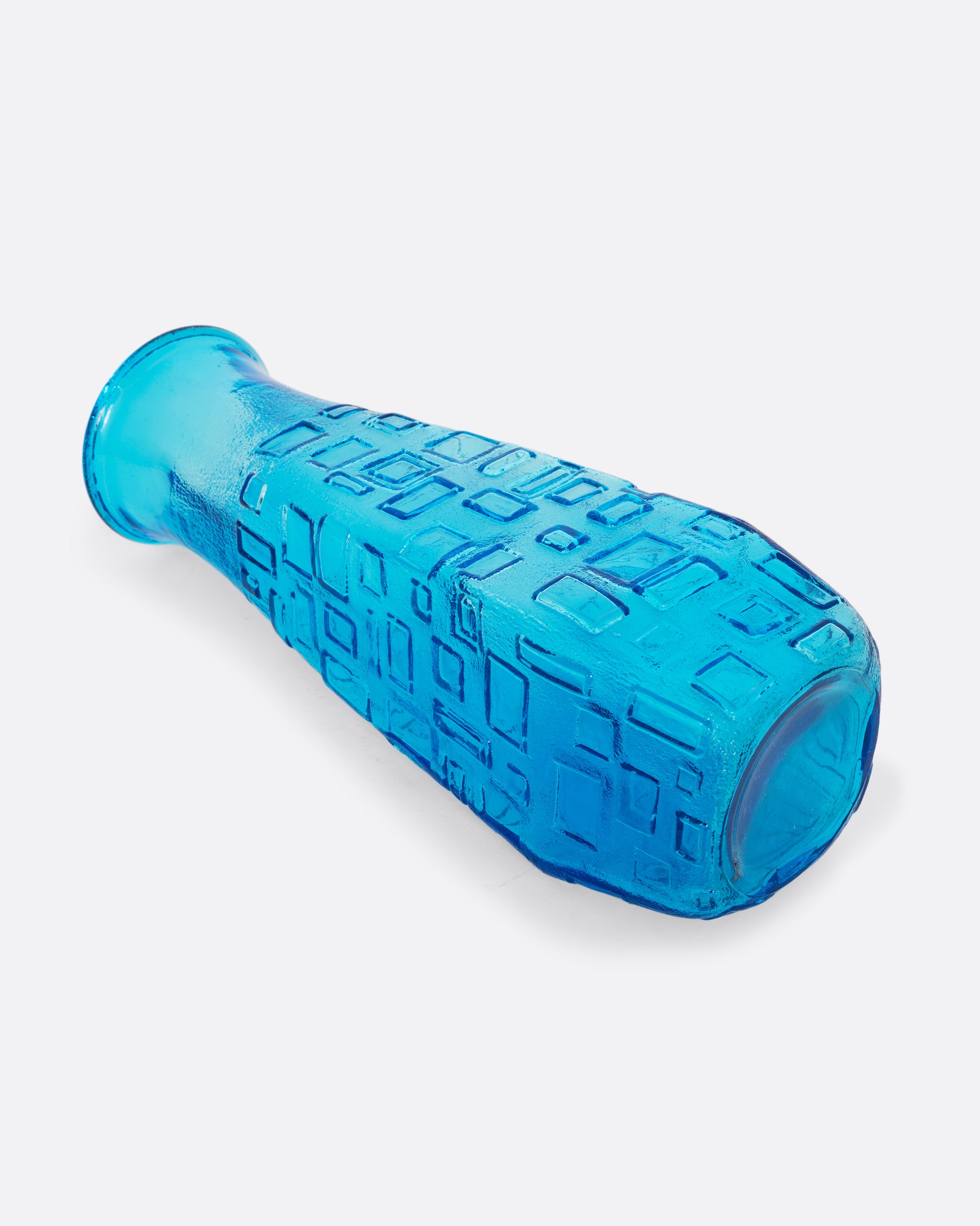  A tall cerulean glass vase with an all-over geometric pattern. Shown diagonally on its side from the side.