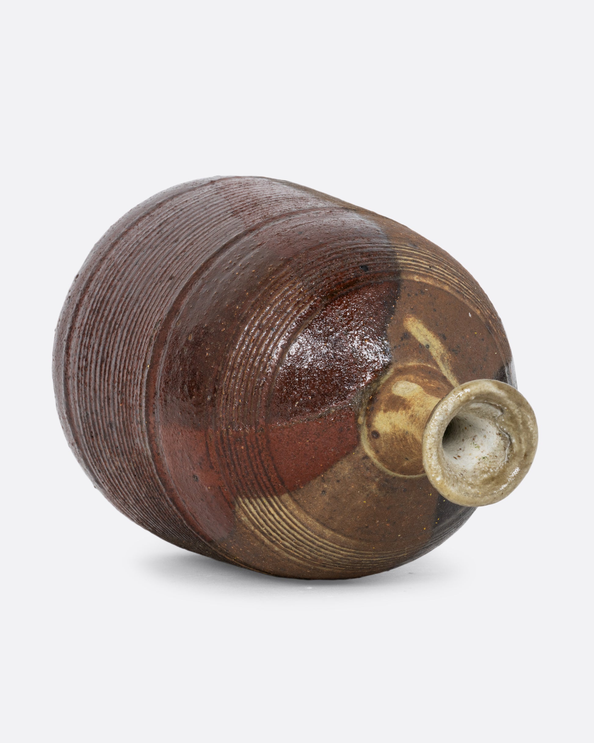 A vase with a brown split contrast glaze and ribbed texture. Shown diagonally on its side from the top.