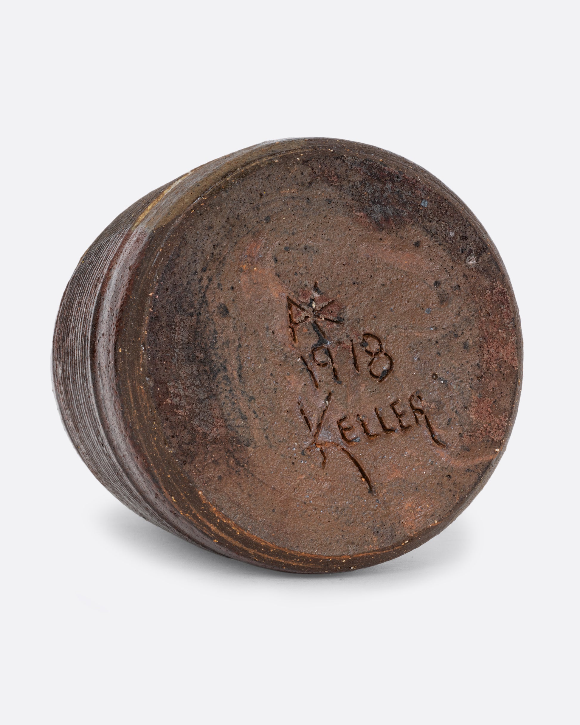 A vase with a brown split contrast glaze and ribbed texture. The artist's signature and 1978 are carved on the bottom. Shown on its side from the bottom.