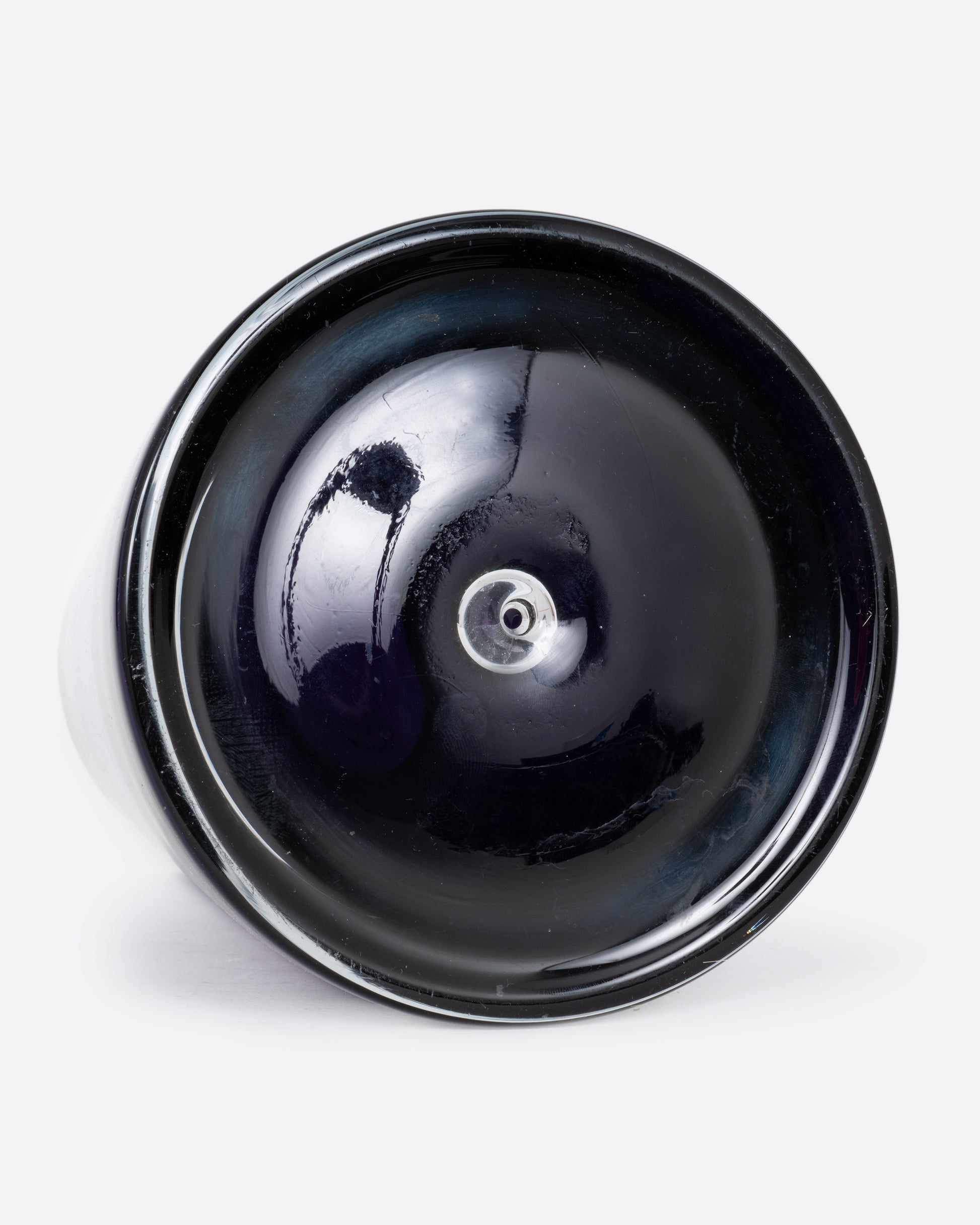 An  aubergine glass vase with a wide base and more narrow top. Shown lying on its side from the bottom.