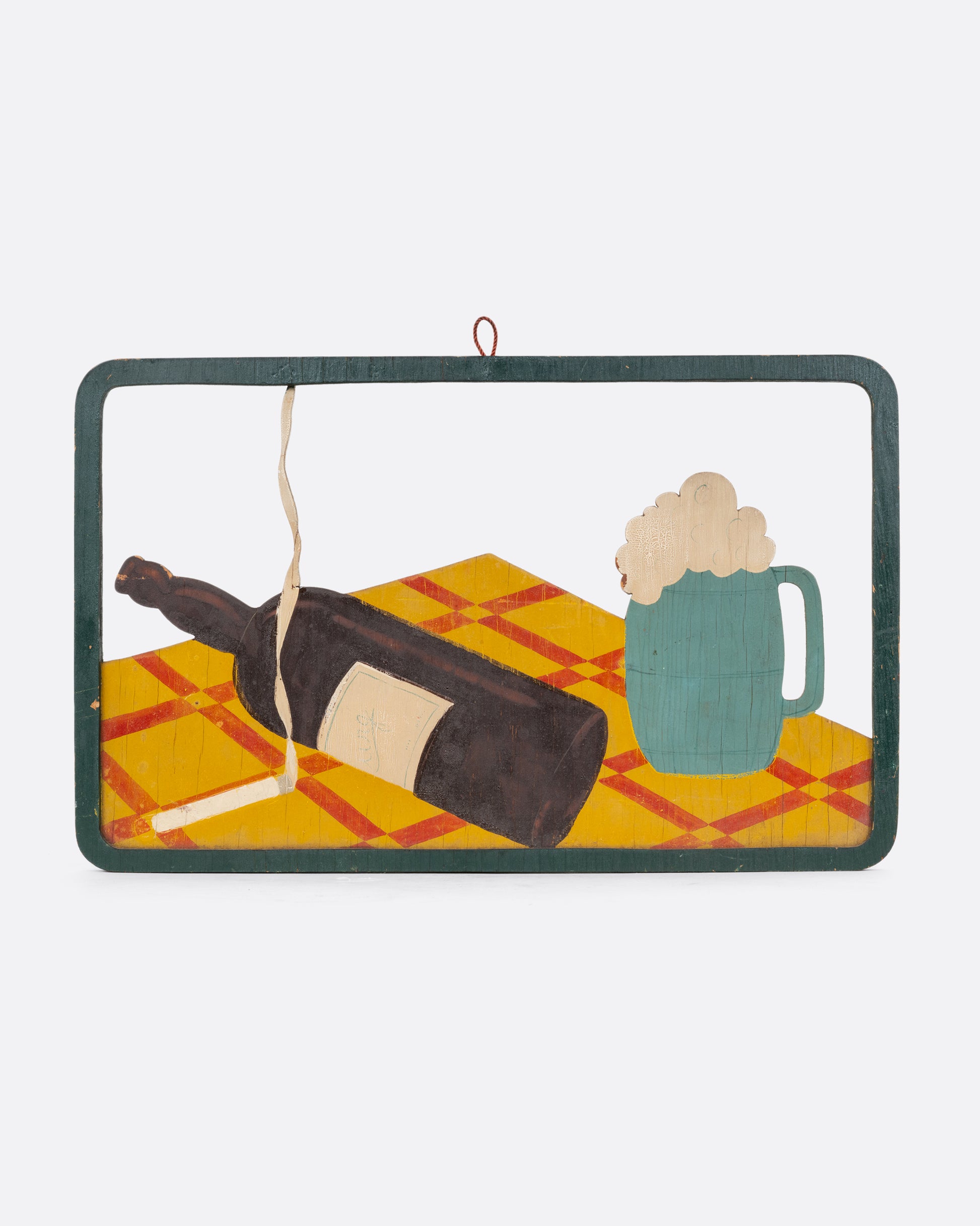 A framed wooden relief still life with a lit cigarette, wine bottle, and beer mug on a table top. Shown from the front.