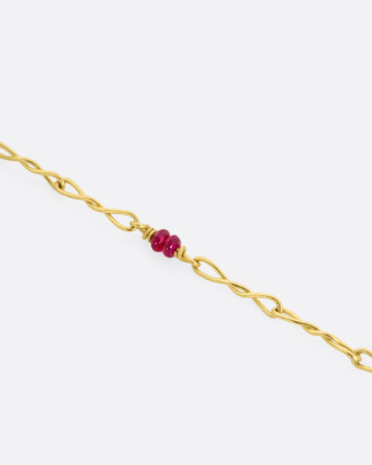 A yellow gold twisted paperclip chain link bracelet with five ruby beads. Shown close up.