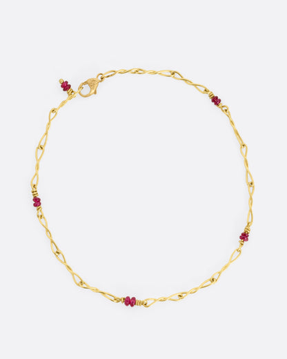 A yellow gold twisted paperclip chain link bracelet with five ruby beads.Shown clasped from the top.