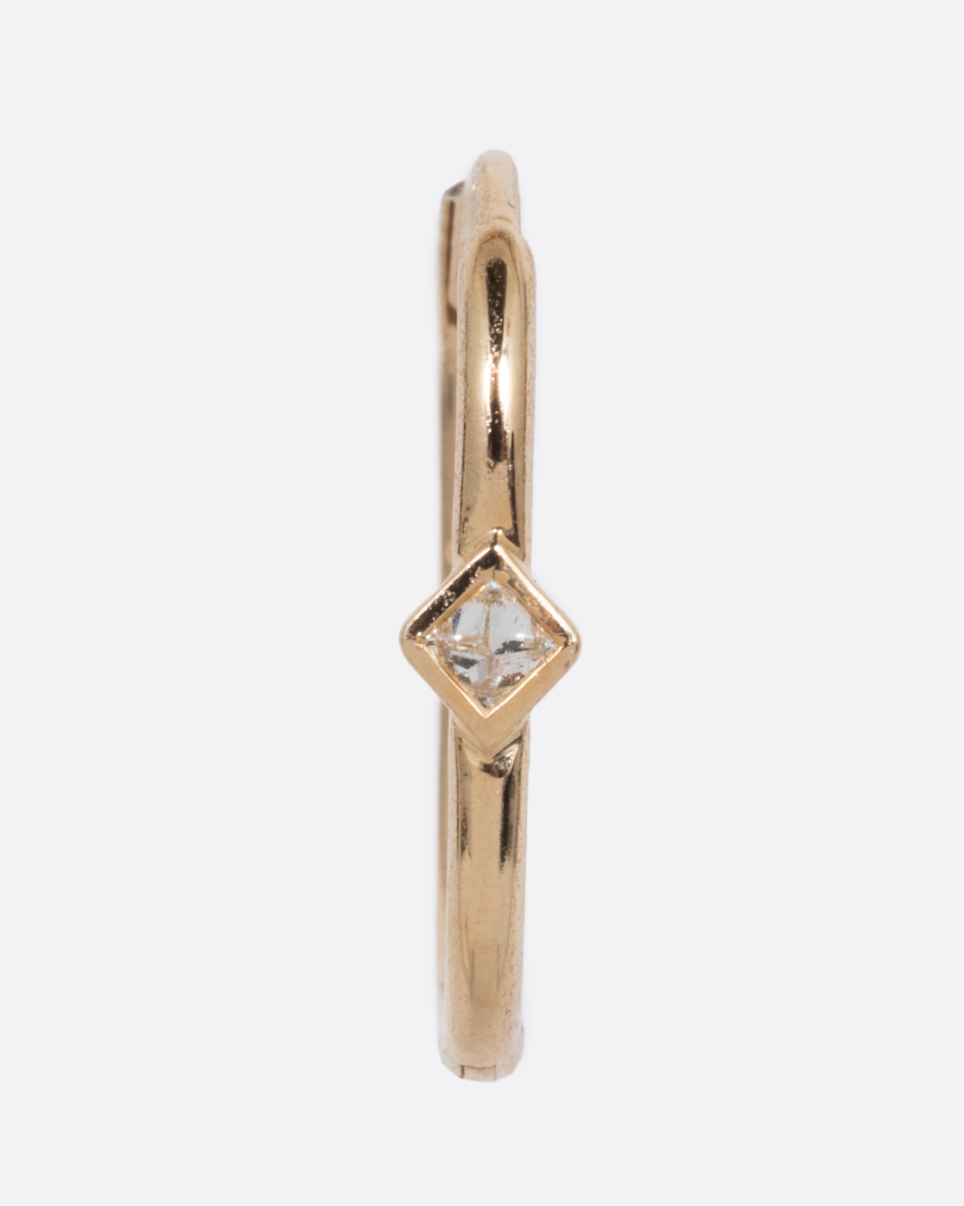 A single yellow gold clicker hoop with a reverse set diamond at the center. Shown from the front.