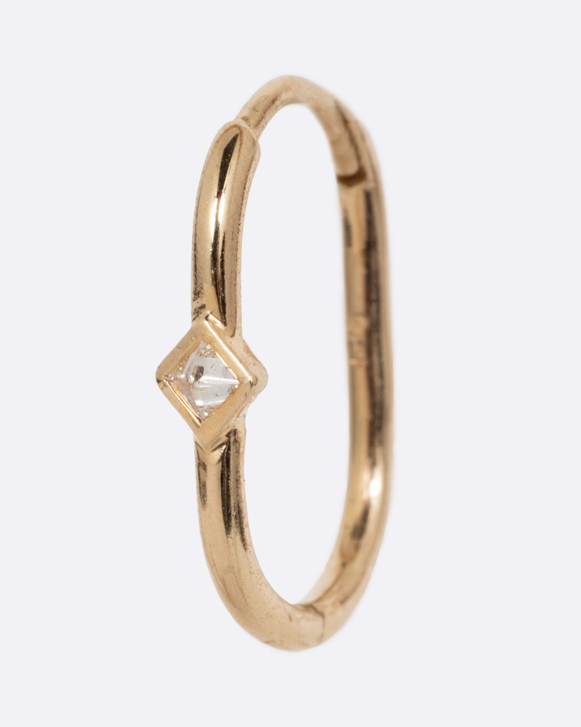 A single yellow gold clicker hoop with a reverse set diamond at the center. Shown from the side.