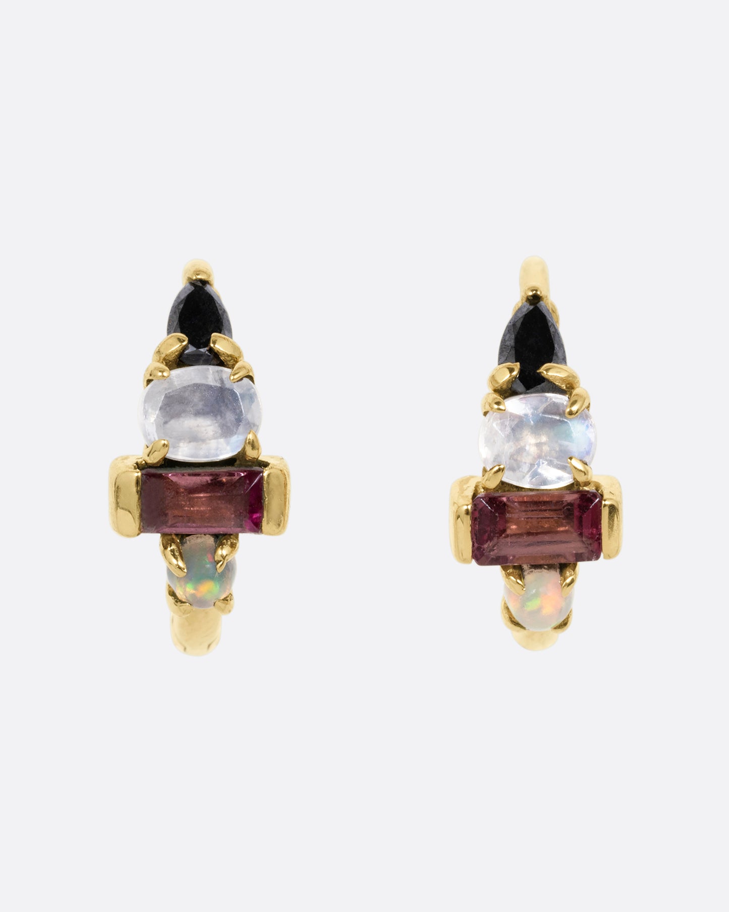 A pair of yellow gold huggie hoops with a gemstone stack of black diamond, moonstone, tourmaline, and opal. Shown from the front.